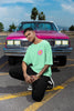 Right side view of a male model wearing an oversized mint green t-shirt with a positive message 