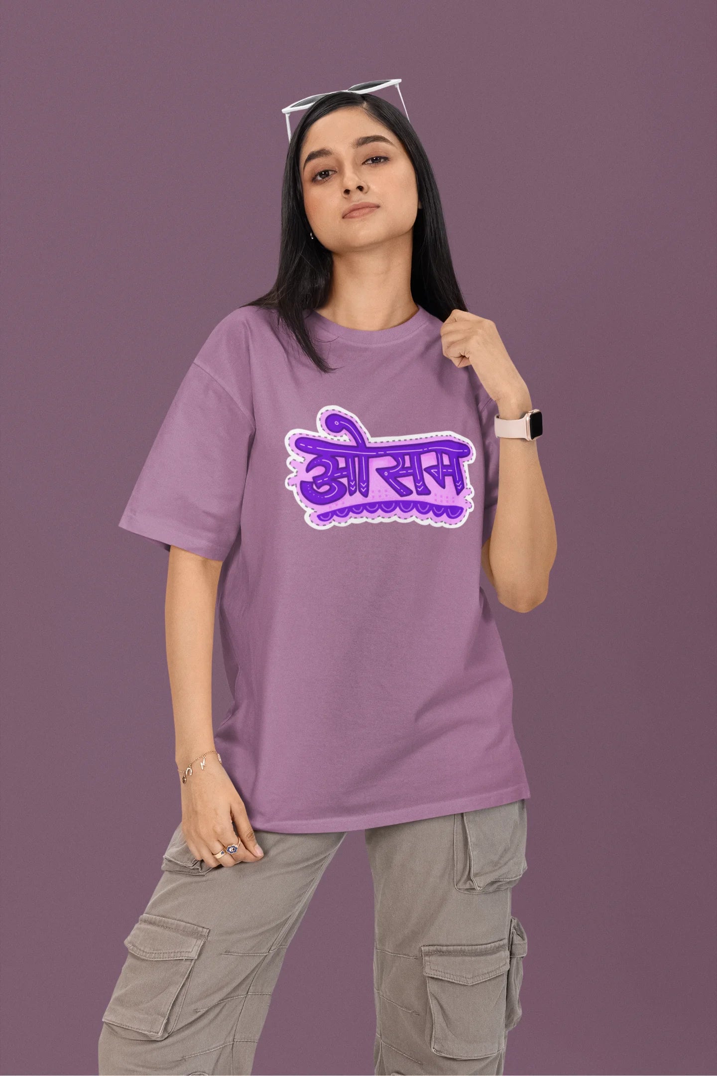 First front view of a female model wearing a dirty purple colored oversized graphic t-shirt featuring the word "awesome" in a Hindi script.