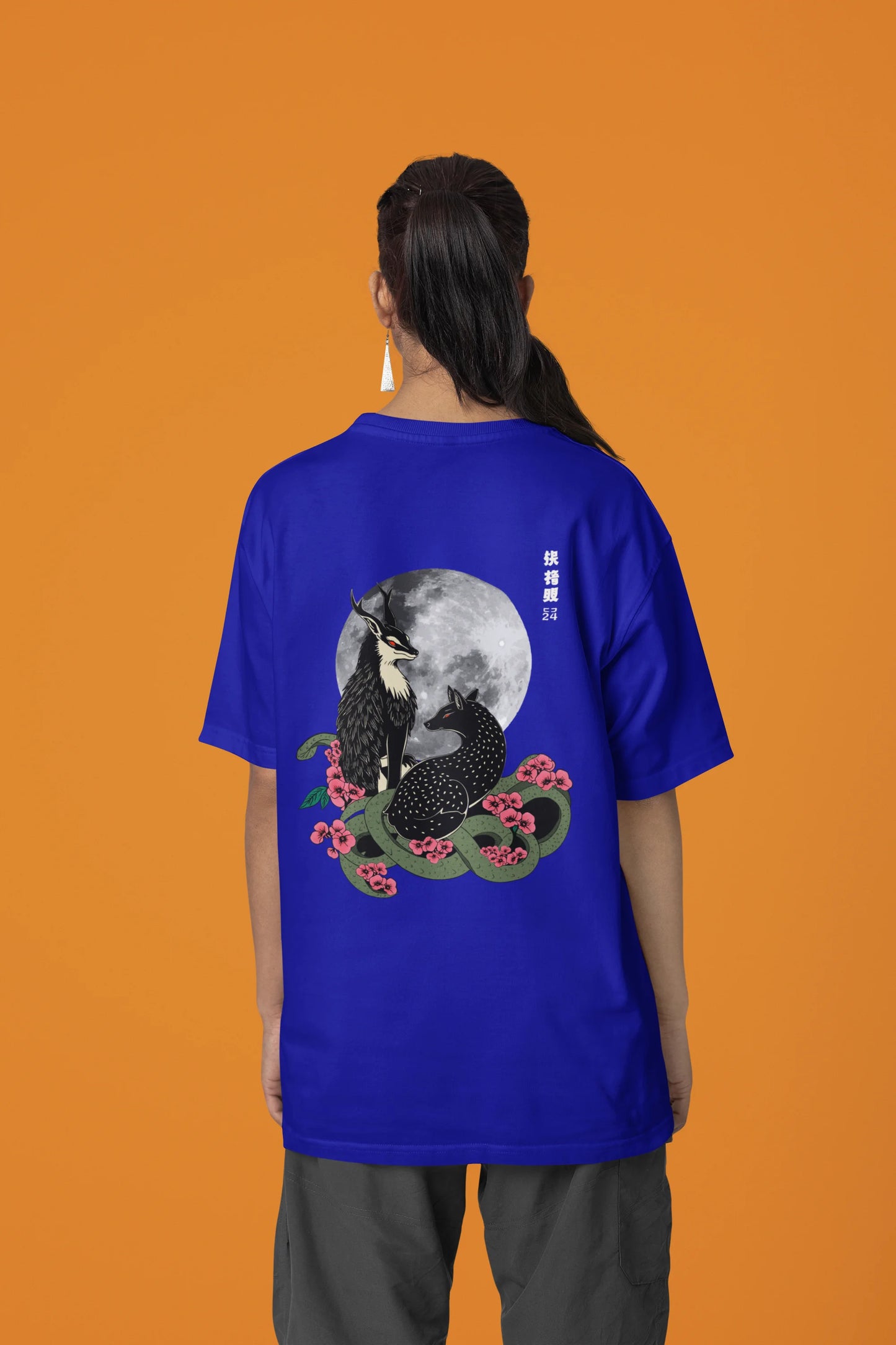 Back view of a female model wearing an oversized royal blue t-shirt featuring a detailed illustration of a gray wolf howling at a full moon in a nighttime setting.