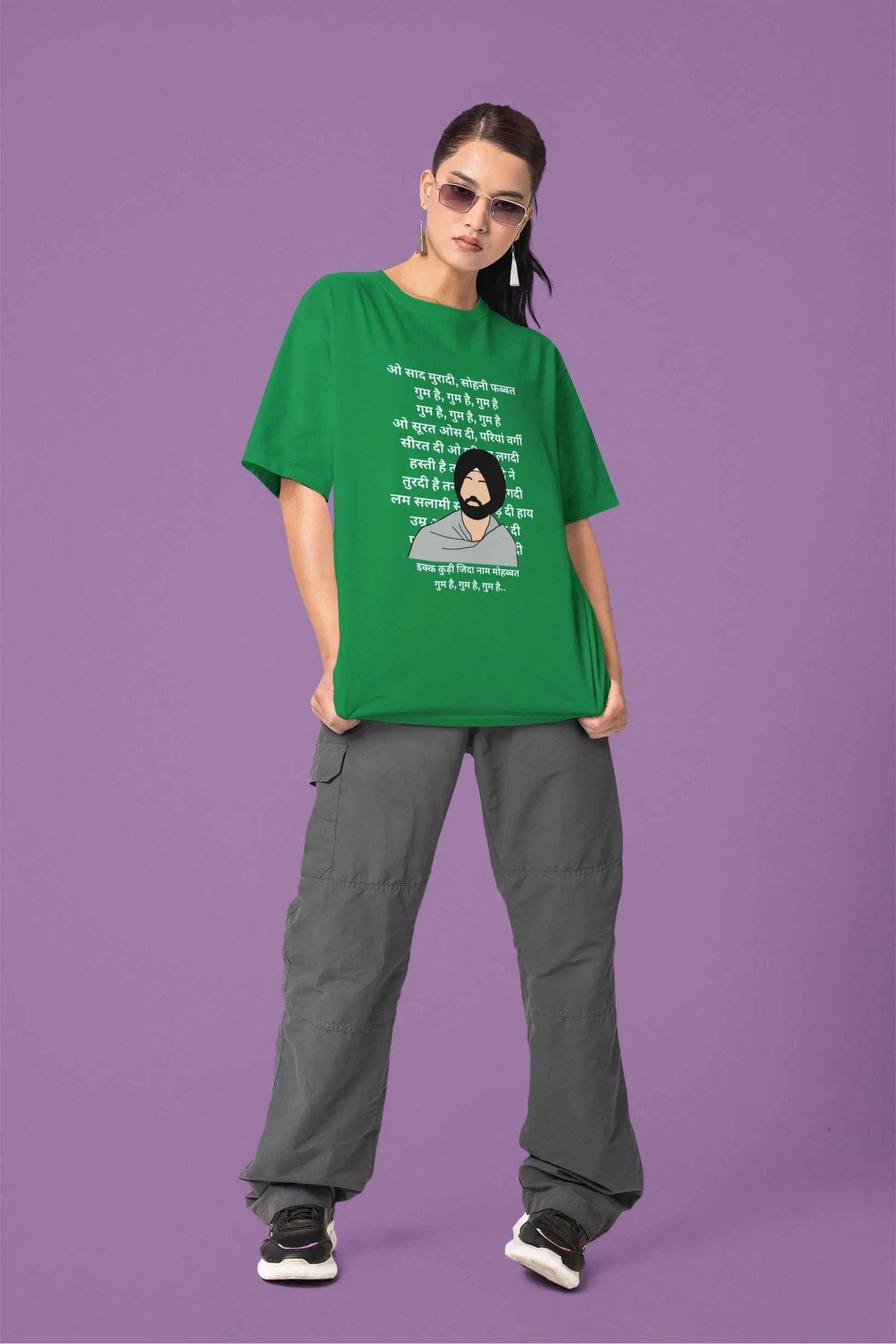 Fourth front view of a female model wearing a forest green oversized  T-shirt with a Diljit Dosanjh portrait  with lyrics from the song "Ikk Kudi" in the background.