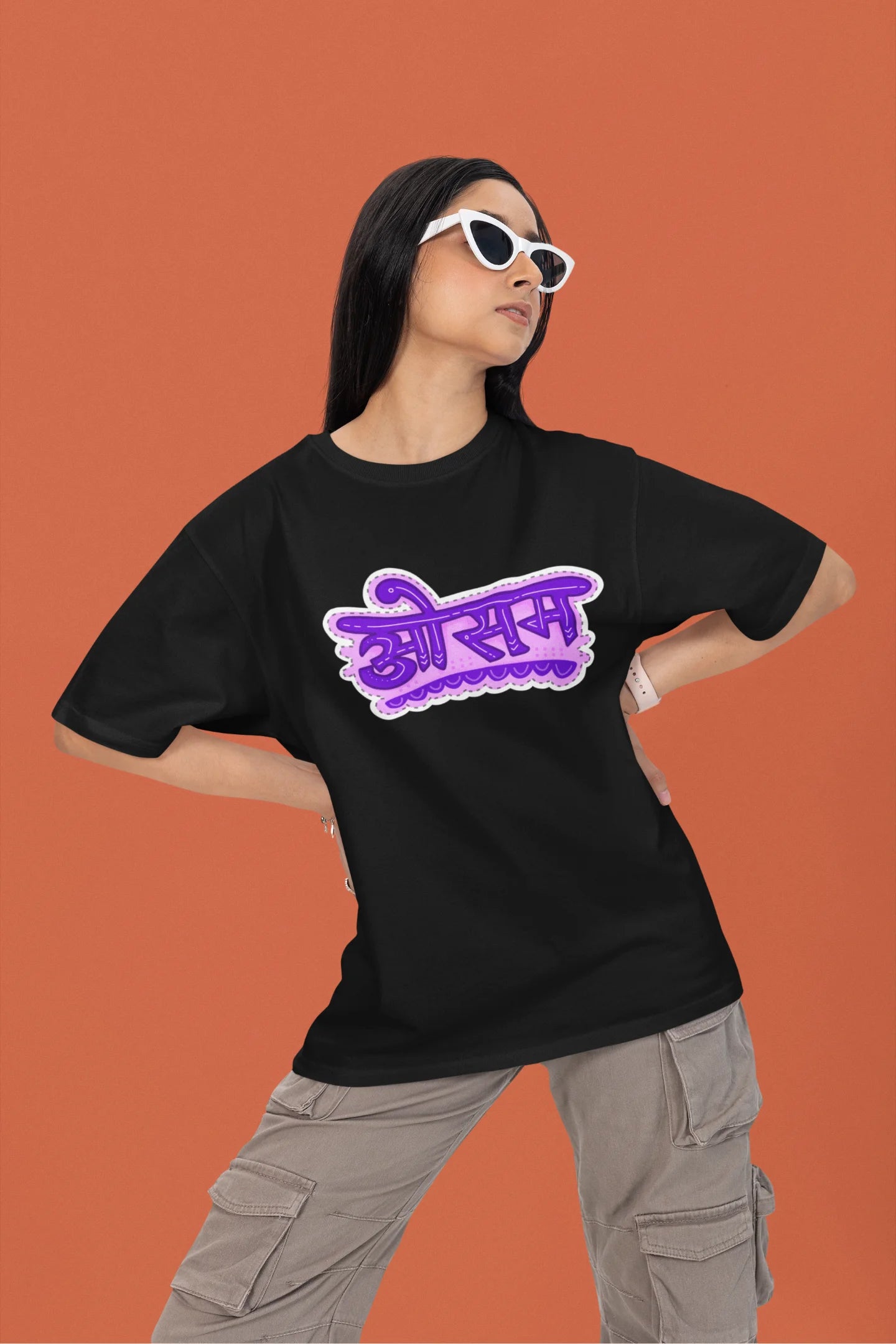 2nd front view of a female model wearing a black colored oversized graphic t-shirt featuring the word "awesome" in a Hindi script.