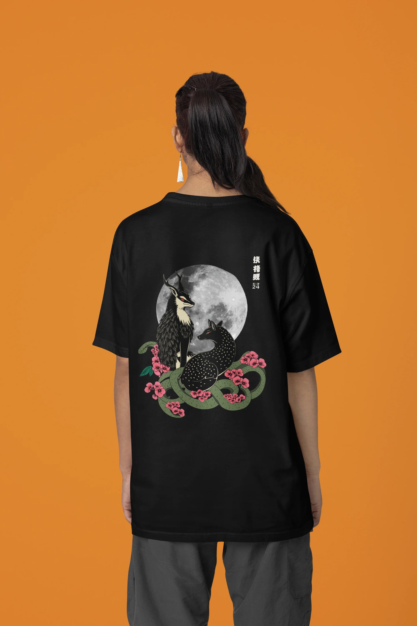 Back view of a female model wearing an oversized black t-shirt featuring a detailed illustration of a gray wolf howling at a full moon in a nighttime setting.