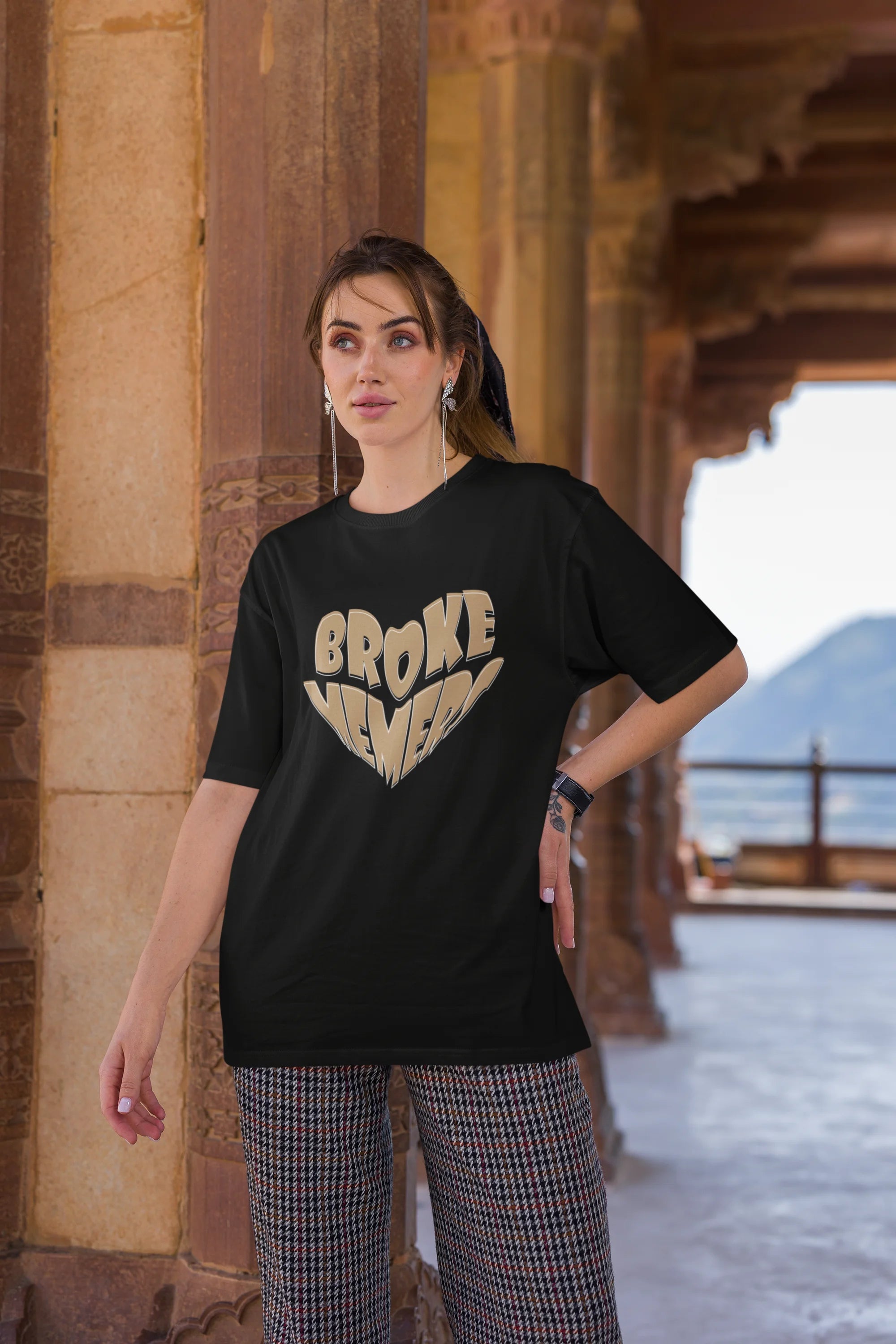 Third front view of female model wearing a black oversized t-shirt featuring the "Broke Memers" logo creatively shaped like a heart. Ideal for fans of Broke Memers who love quality and fashionable clothing.