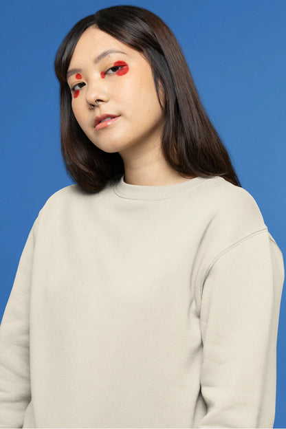 Second front view of female model wearing a cream sweatshirt with a design of a cat dressed as a samurai, standing against a backdrop of waves and a rising sun.