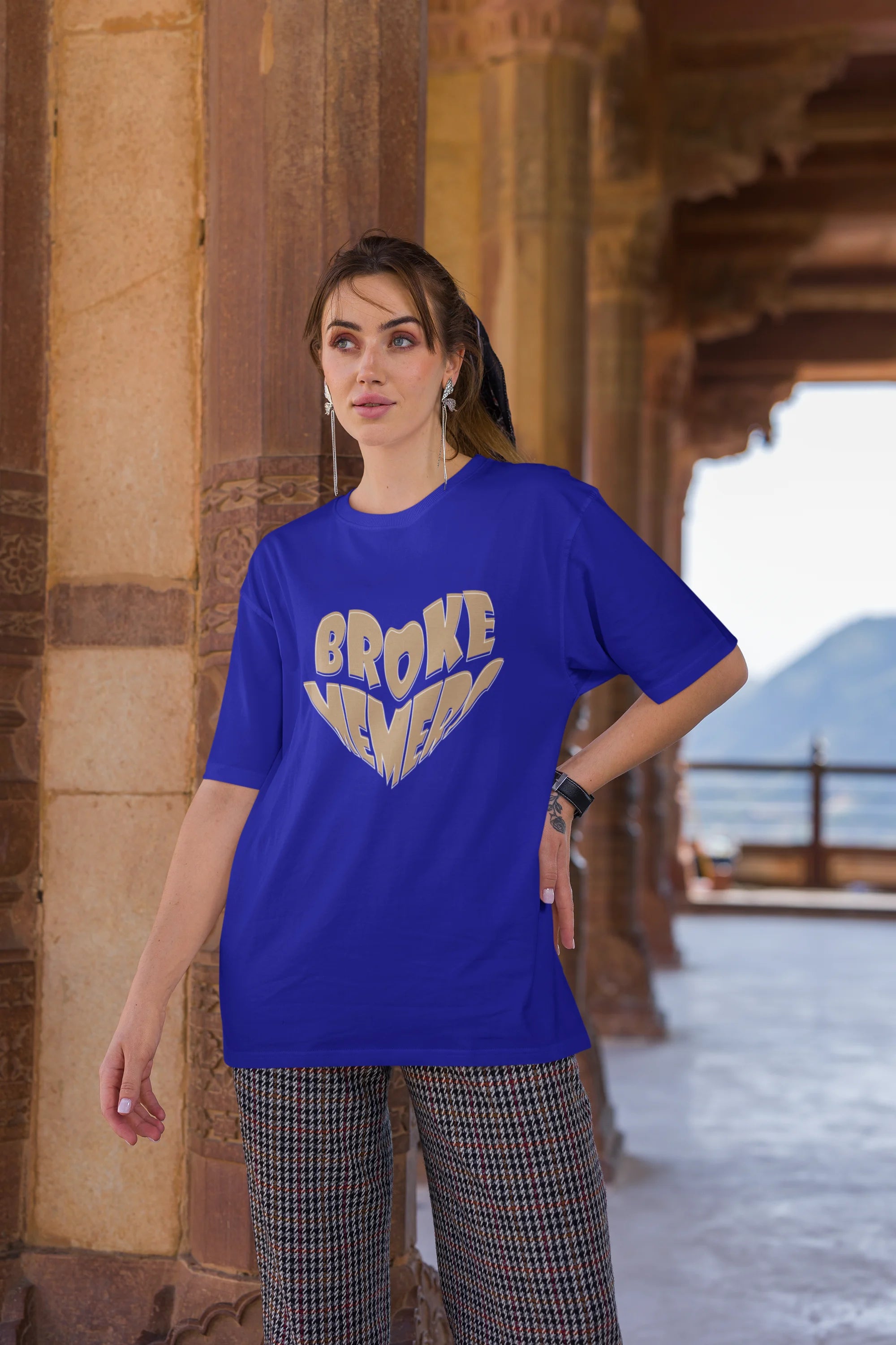 Third front view of female model wearing a royal blue oversized t-shirt featuring the "Broke Memers" logo creatively shaped like a heart. Ideal for fans of Broke Memers who love quality and fashionable clothing.