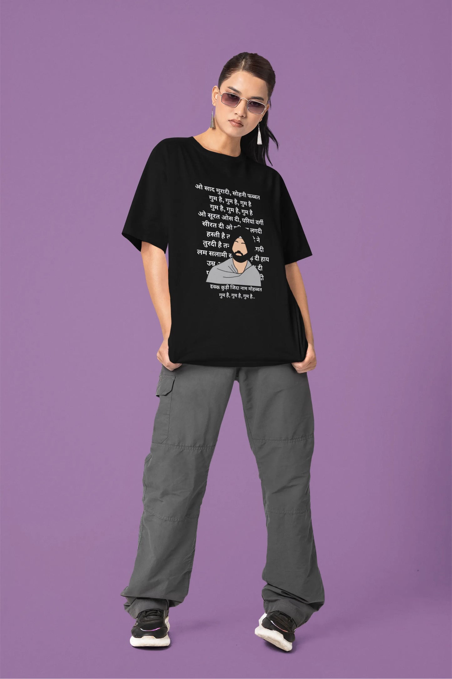 Fifth front view of a female model wearing a black oversized  T-shirt with a Diljit Dosanjh portrait  with lyrics from the song "Ikk Kudi" in the background.