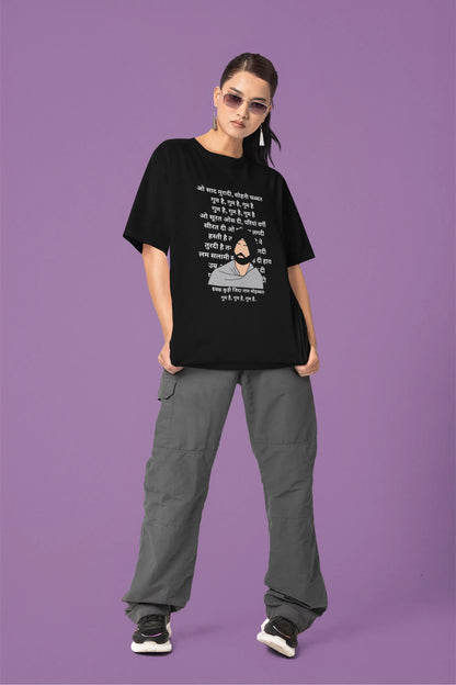 Fifth front view of a female model wearing a black oversized  T-shirt with a Diljit Dosanjh portrait  with lyrics from the song "Ikk Kudi" in the background.