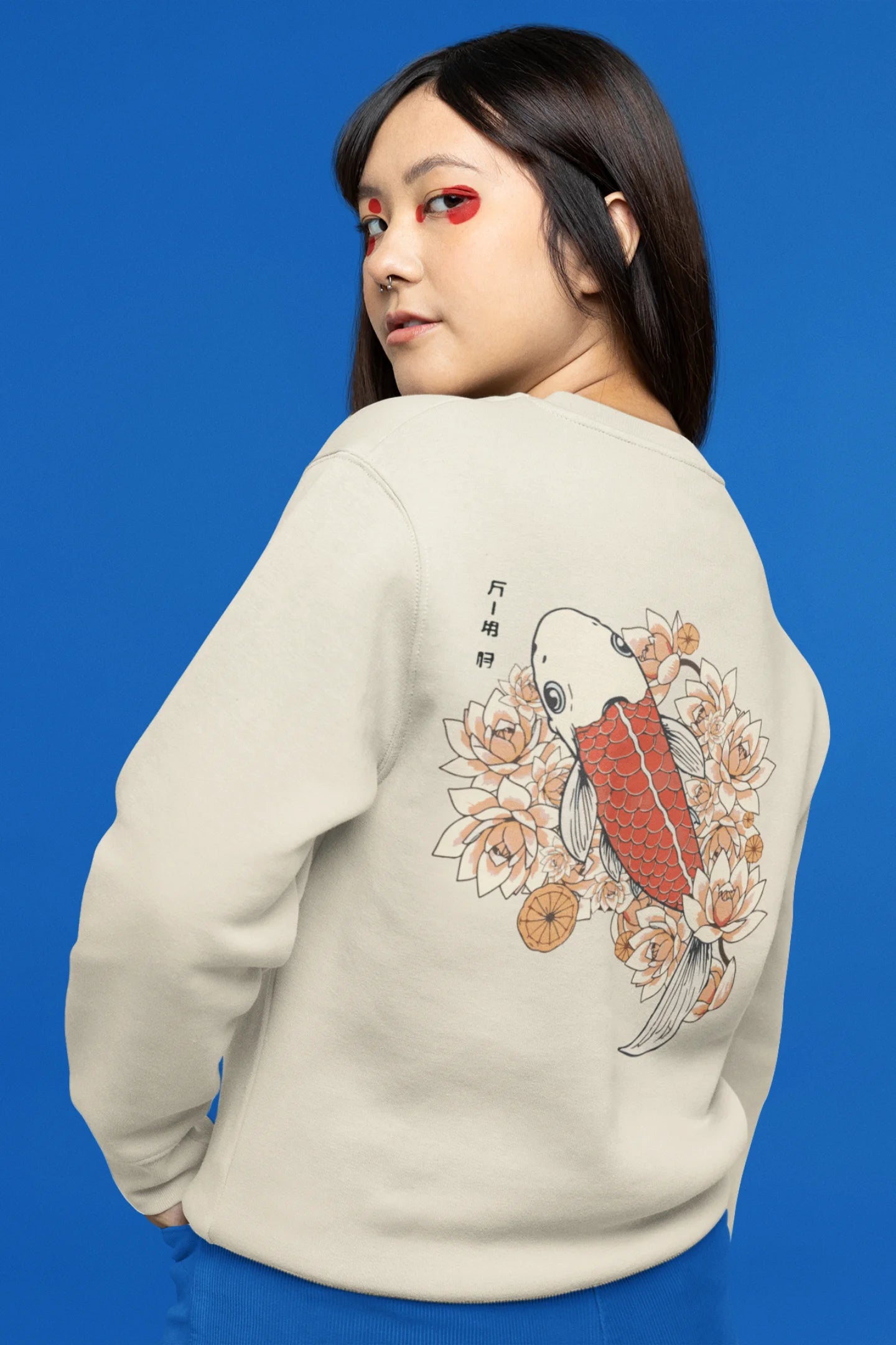 Back view of a female model wearing a cream sweatshirt  with a design of a koi fish swimming in a bed of flowers.