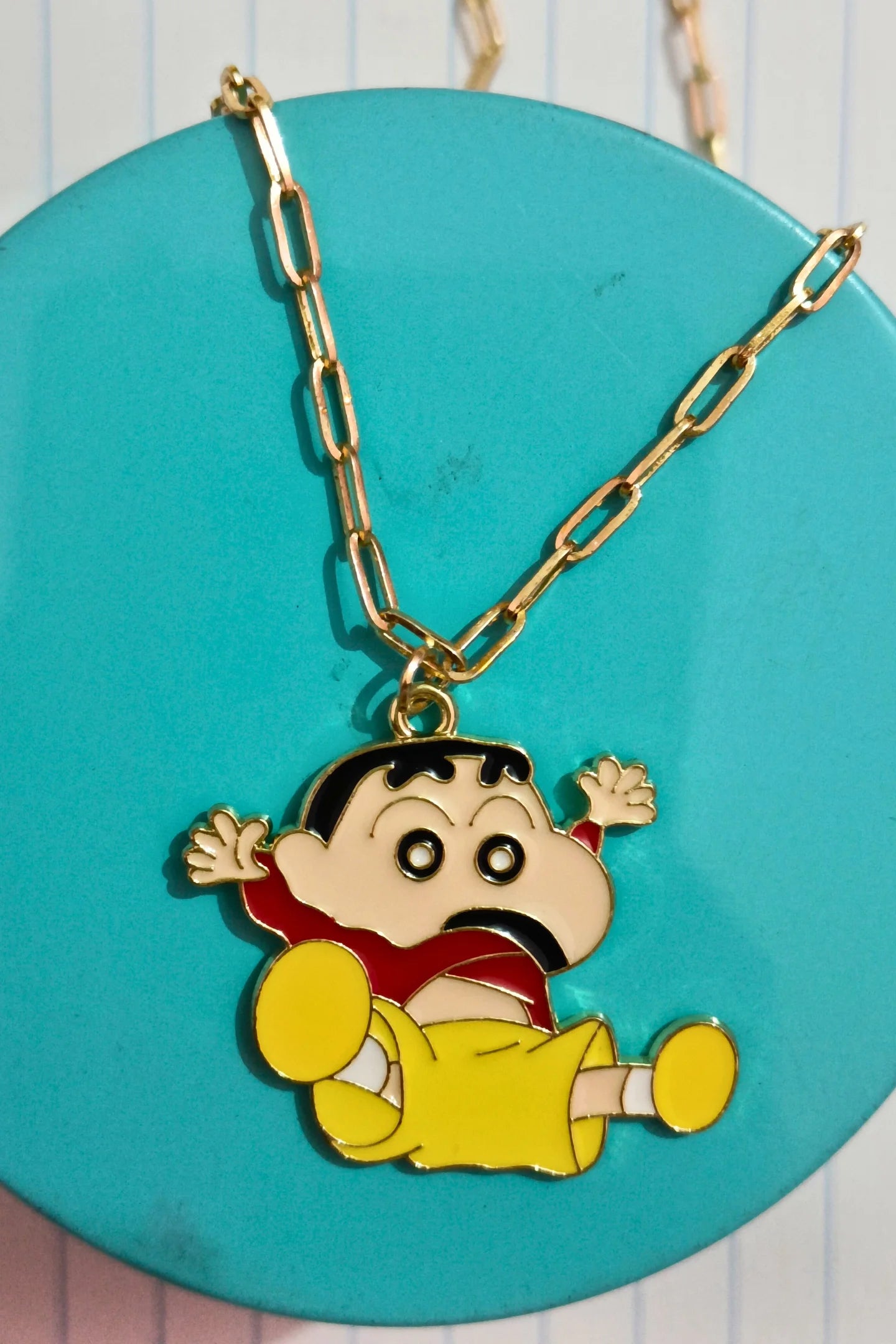 3rd view of a gold chain necklace with a small pendant depicting Shin Chan jumping in the air and shouting "Hurray!