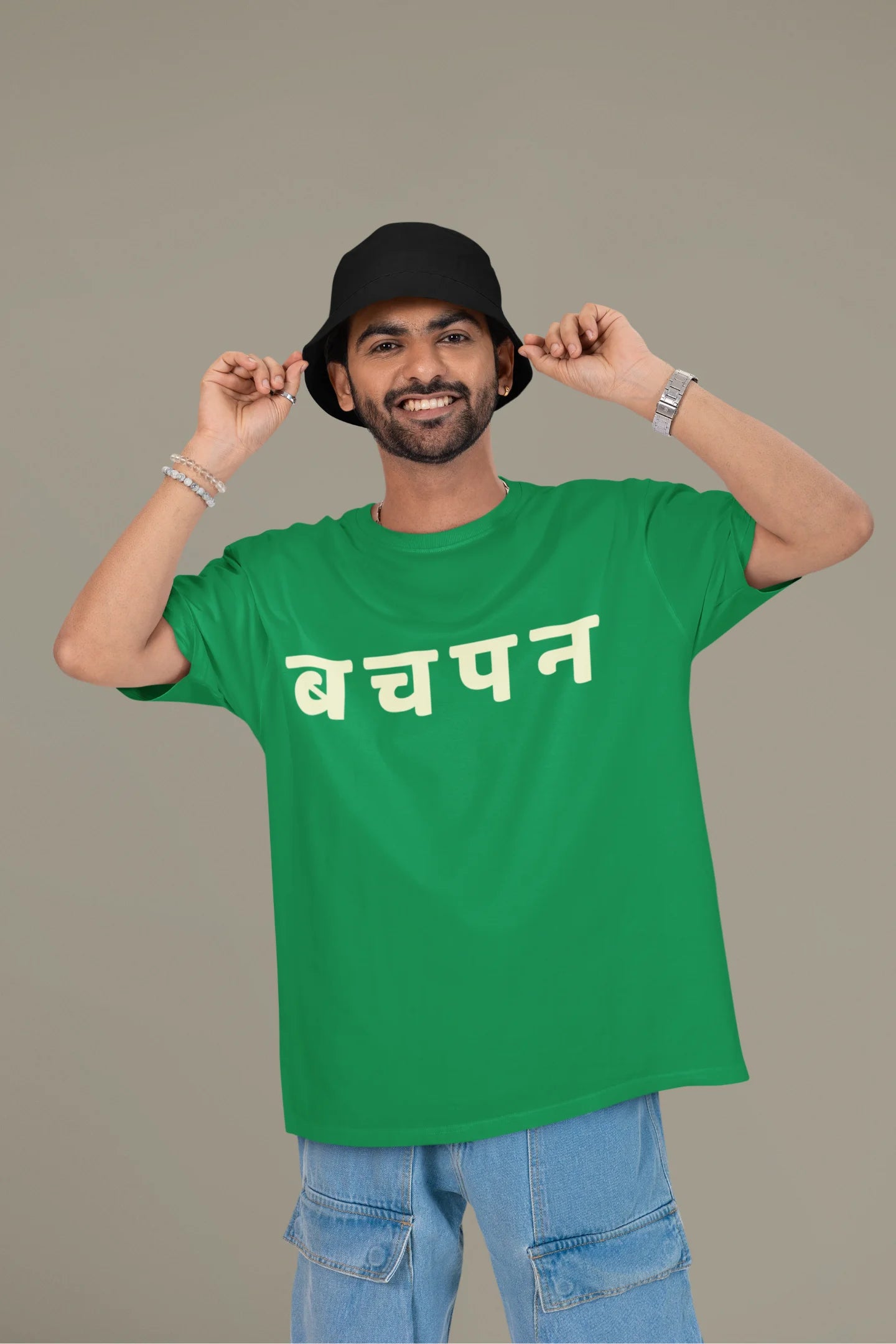 First front view of a male model wearing a forest green oversized t-shirt featuring a collage of illustrations or symbols representing various childhood games commonly played by kids in India.