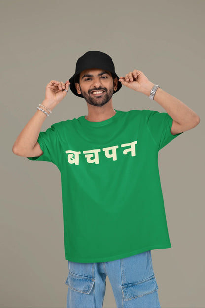 First front view of a male model wearing a forest green oversized t-shirt featuring a collage of illustrations or symbols representing various childhood games commonly played by kids in India.