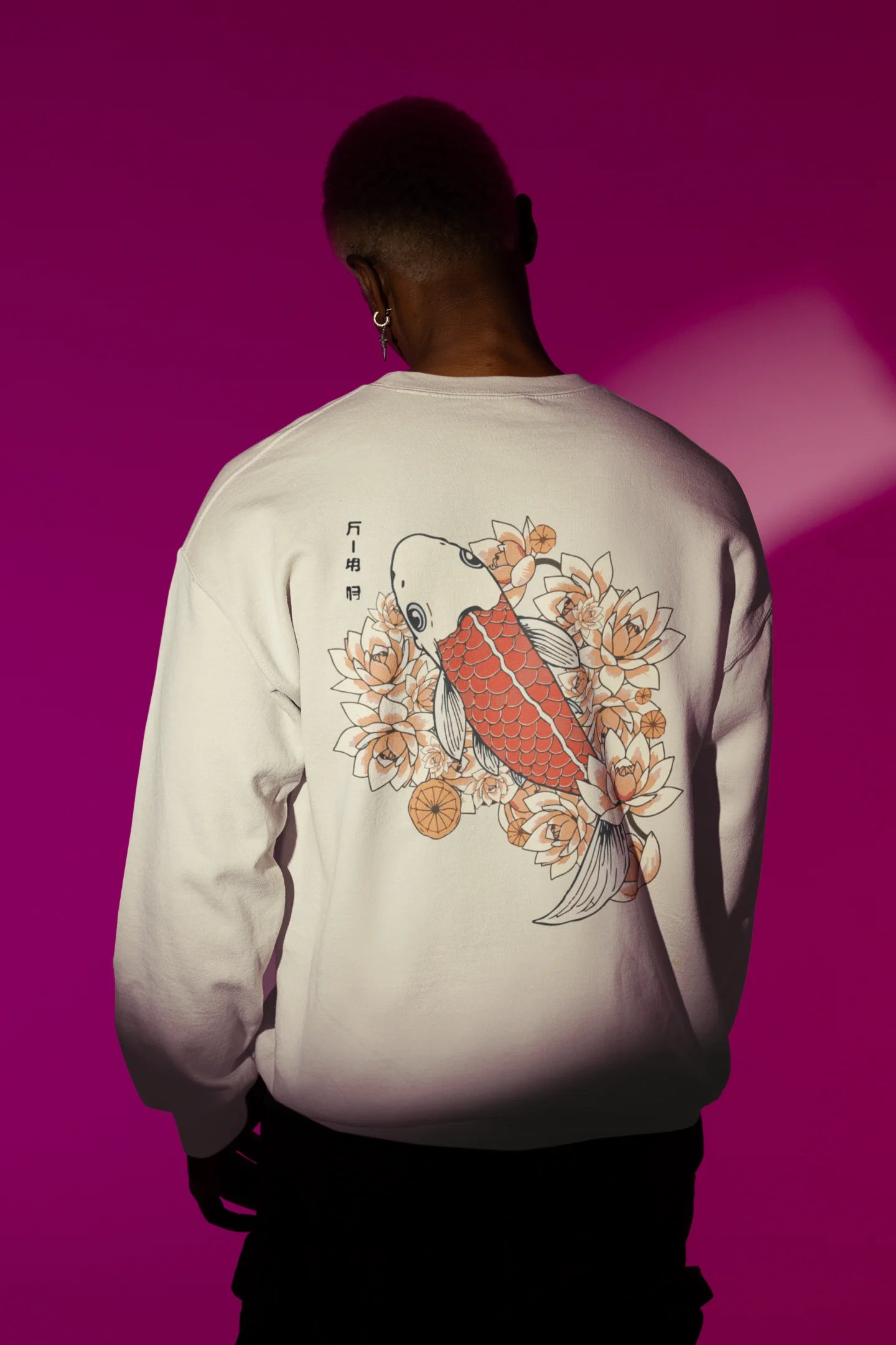 Back view of a male model wearing a cream sweatshirt  with a design of a koi fish swimming in a bed of flowers.
