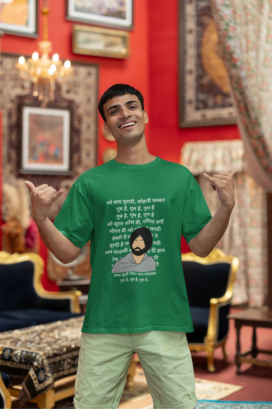 Second front view of a male model wearing a forest green oversized  T-shirt with a Diljit Dosanjh portrait  with lyrics from the song "Ikk Kudi" in the background.