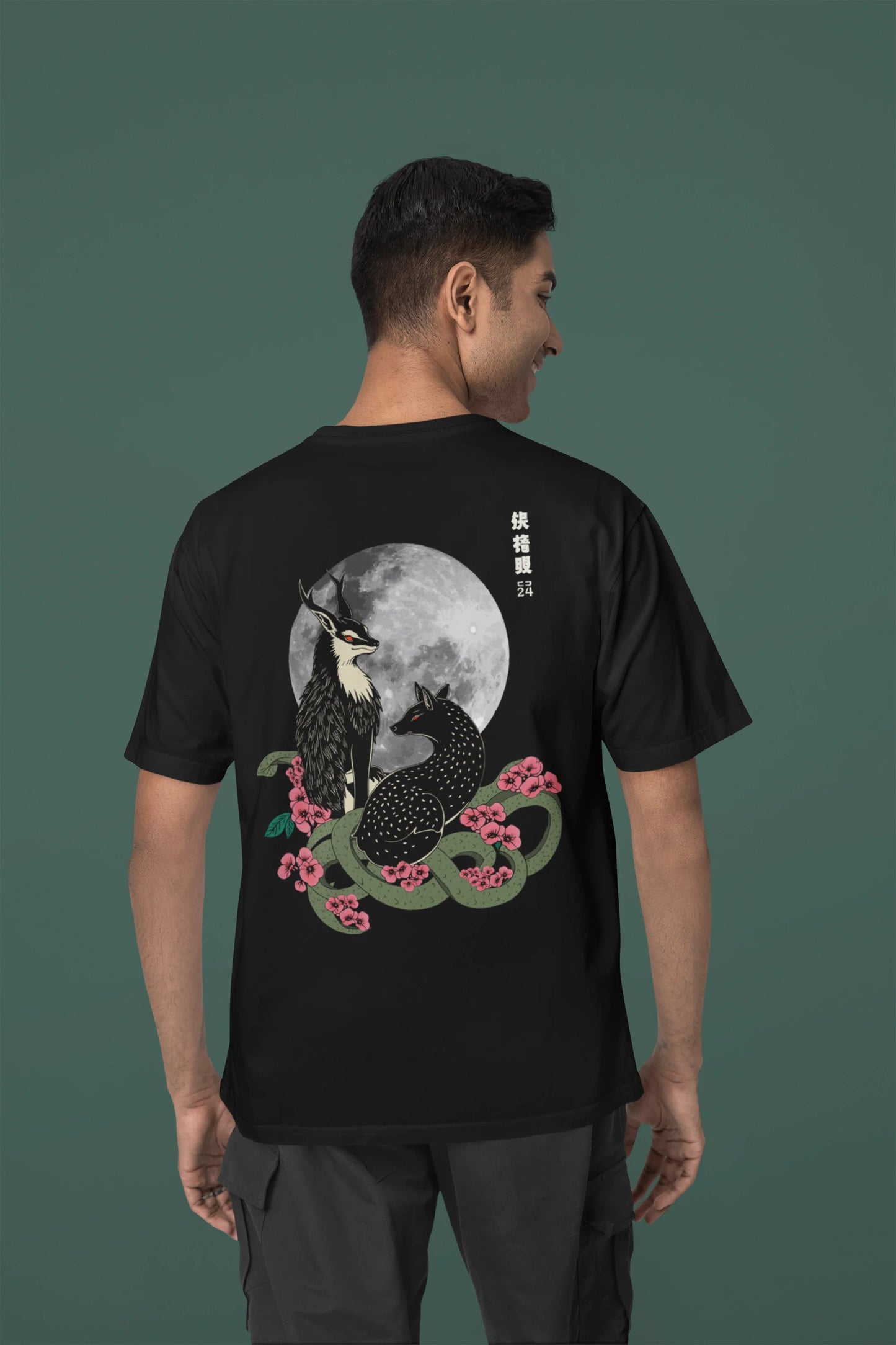 Back view of a male model wearing an oversized black t-shirt featuring a detailed illustration of a gray wolf howling at a full moon in a nighttime setting.