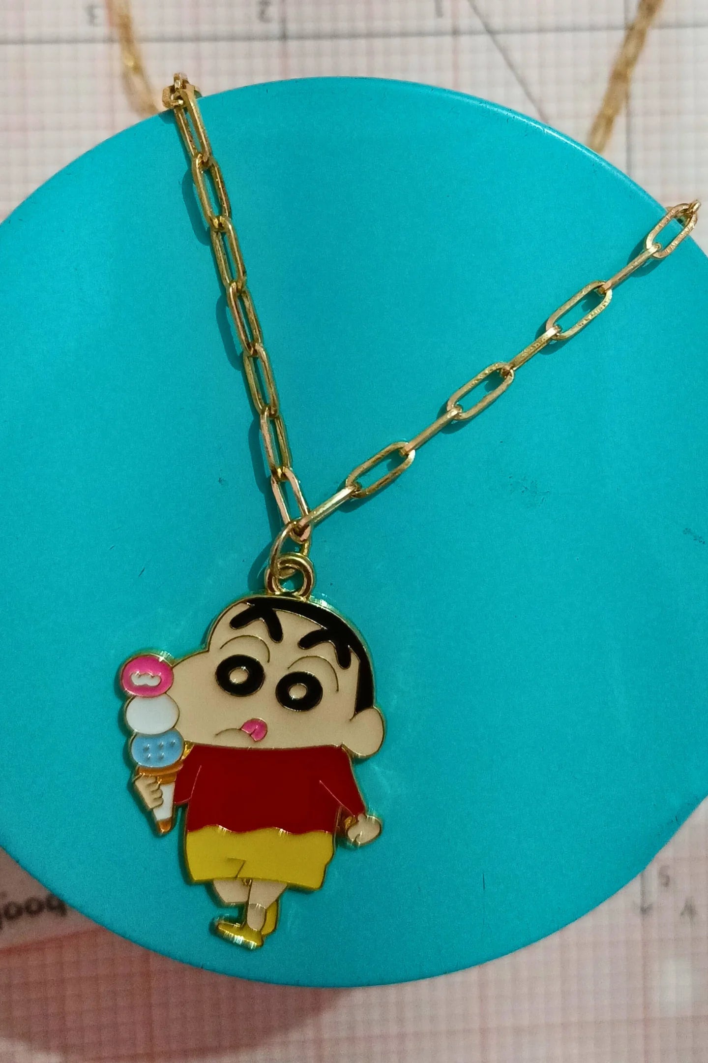3rd view of a gold chain necklace with a small pendant depicting Shin Chan eating ice cream.