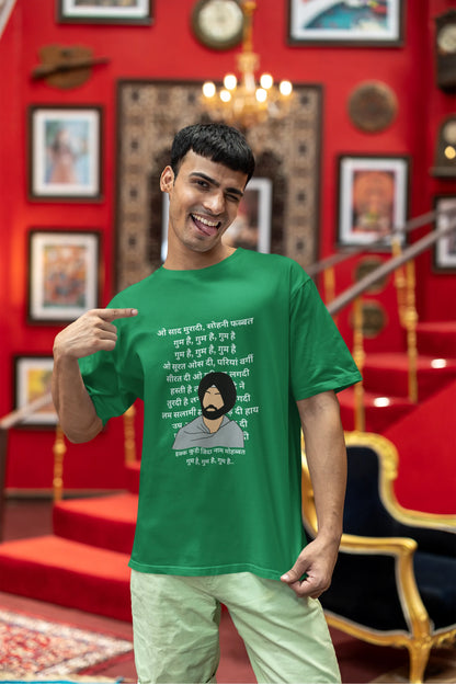 Third front view of a male model wearing a forest green oversized  T-shirt with a Diljit Dosanjh portrait  with lyrics from the song "Ikk Kudi" in the background.
