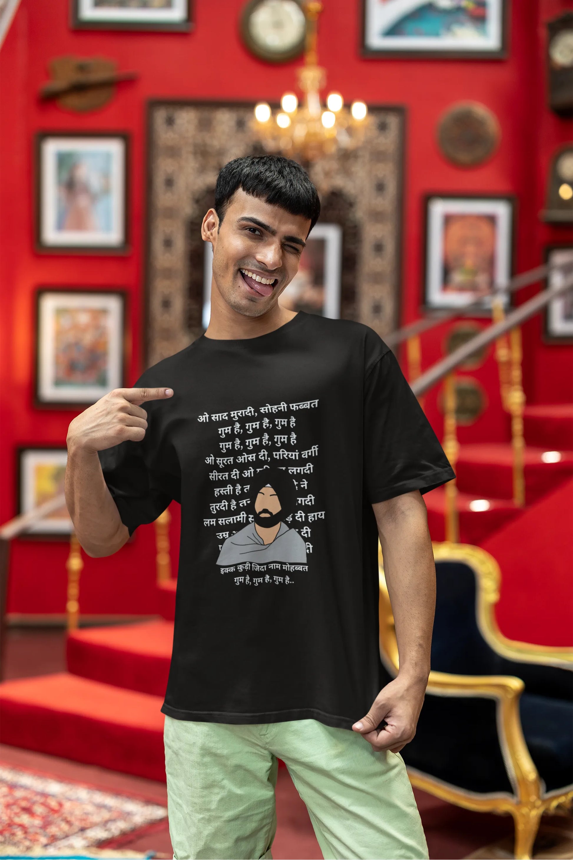 First front view of a male model wearing a black oversized  T-shirt with a Diljit Dosanjh portrait  with lyrics from the song "Ikk Kudi" in the background.
