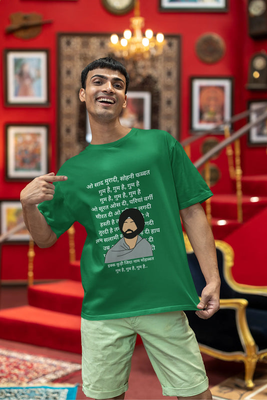 First front view of a male model wearing a forest green oversized  T-shirt with a Diljit Dosanjh portrait  with lyrics from the song "Ikk Kudi" in the background.
