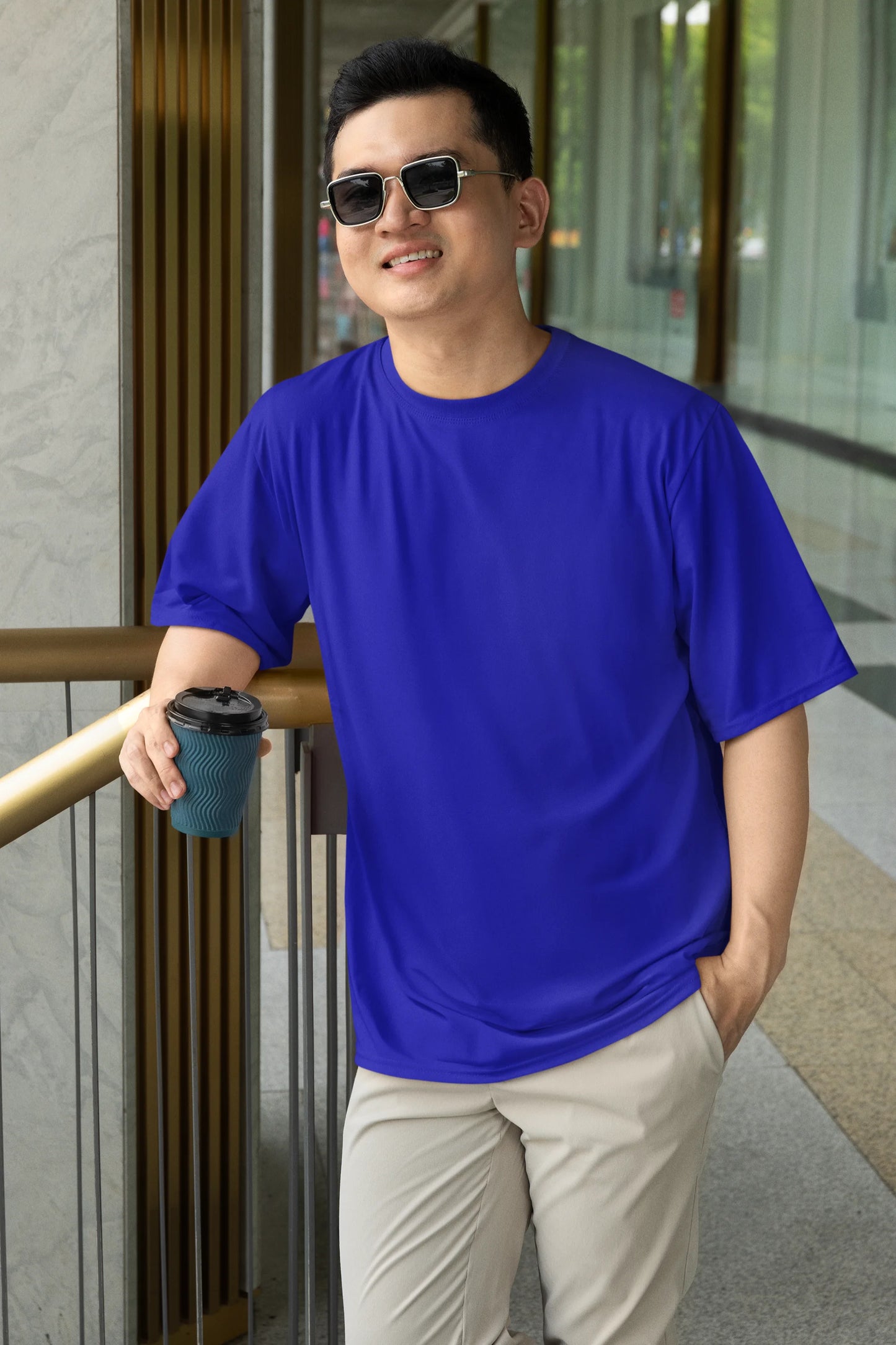 Front view of a male model wearing a royal blue oversized tee with a design of a cat dressed as a samurai, standing against a backdrop of waves and a rising sun.