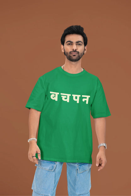 2nd front view of a male model wearing a forest green oversized t-shirt featuring a collage of illustrations or symbols representing various childhood games commonly played by kids in India.