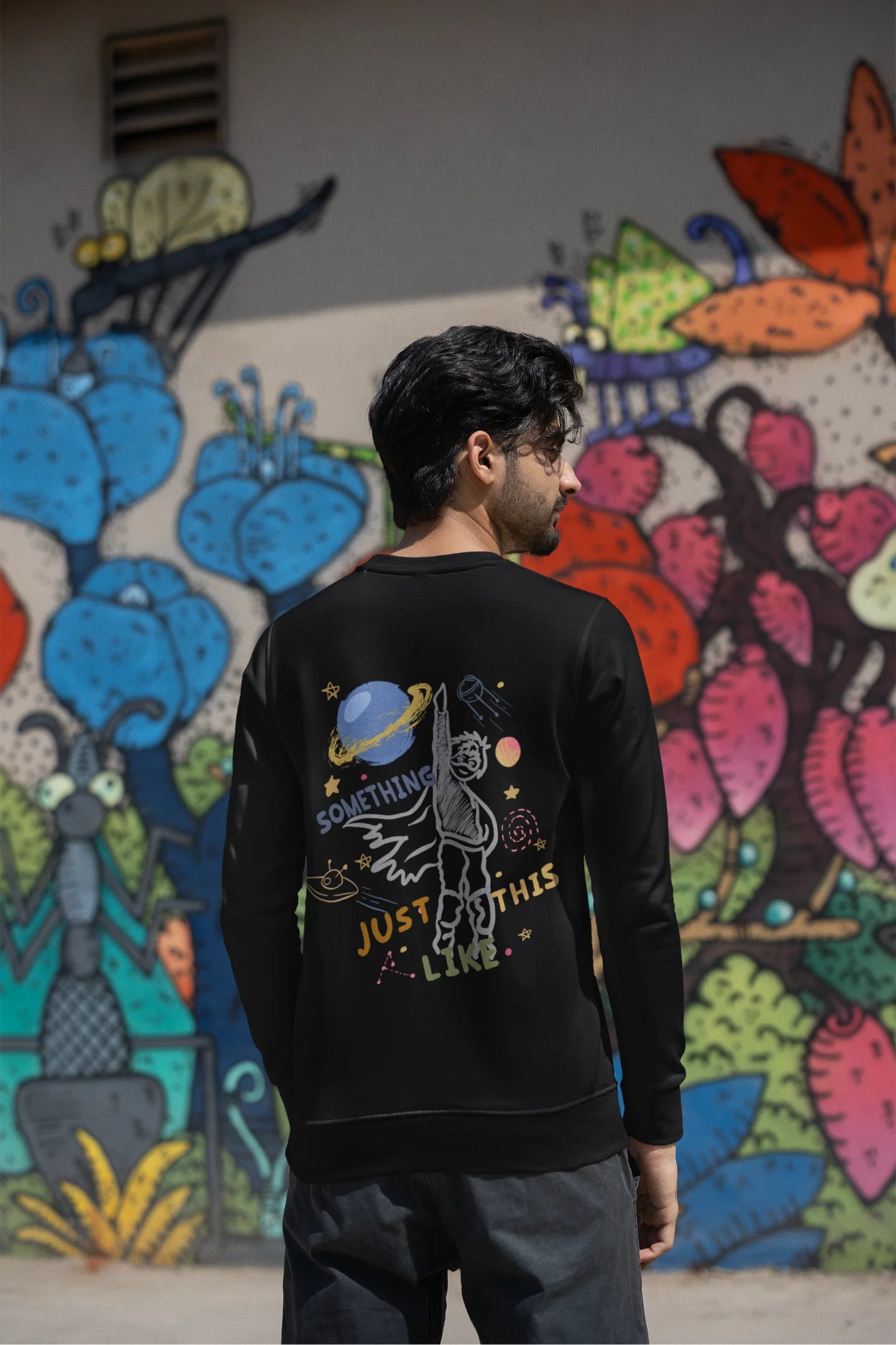 Back view of a male model wearing an black sweatshirt with a design inspired by the "Something Just Like This" music video, featuring the word "Superheroes".