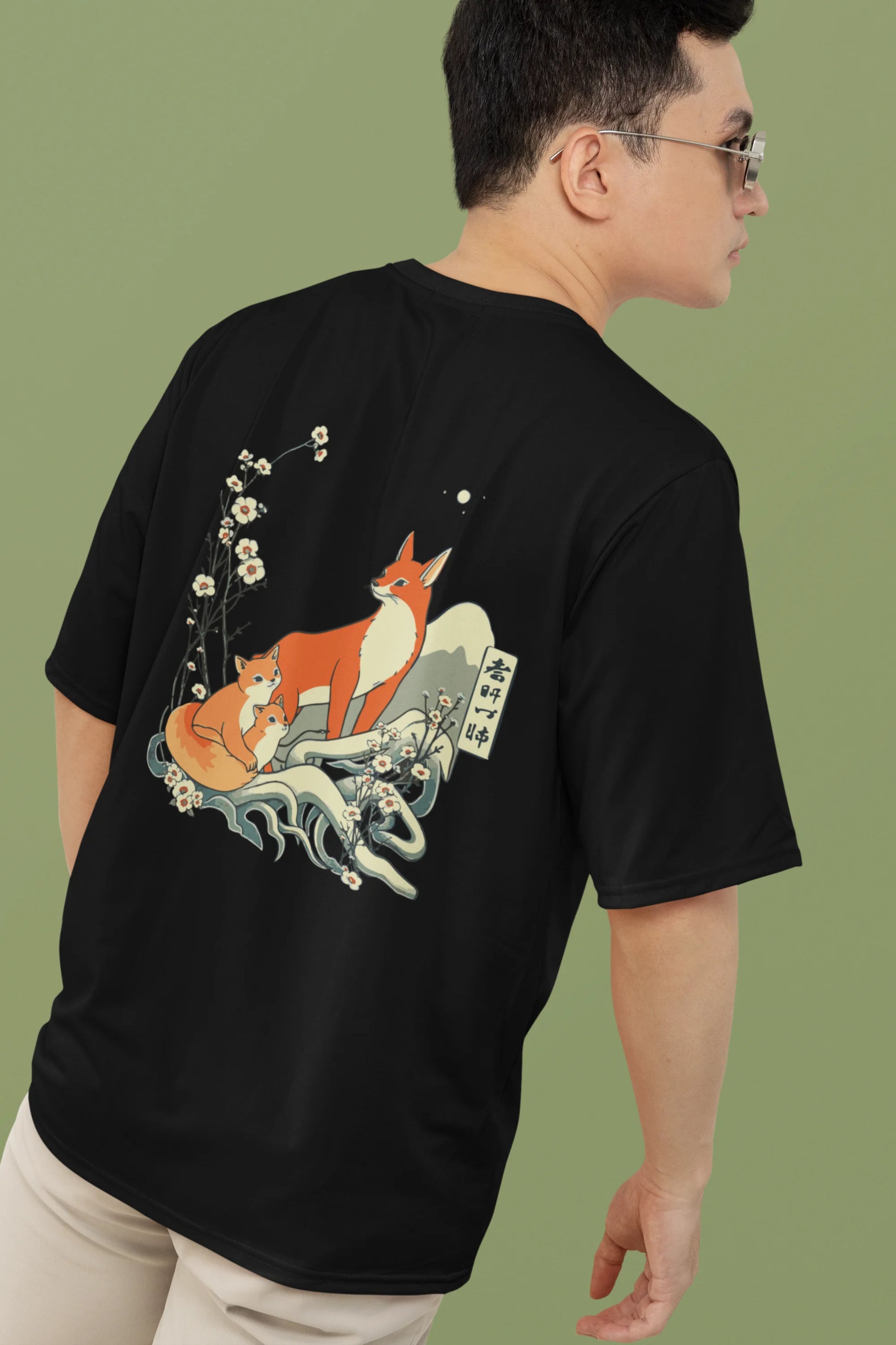 2nd back view of a male model wearing a black oversized tee with a design of a fox and its cub in a traditional Japanese landscape.