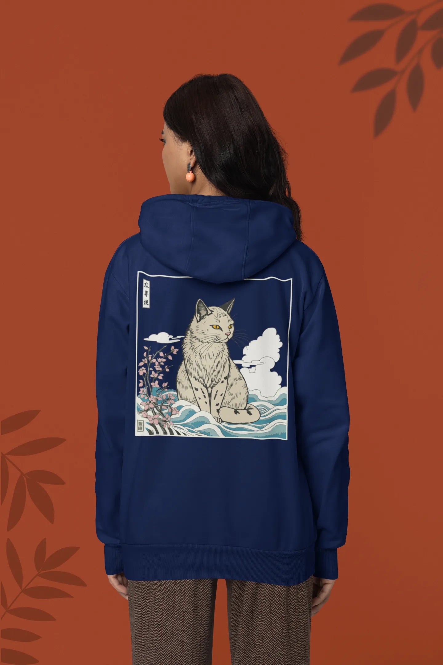 Back view of a female model wearing a navy blue hoodie with a design of a wildcat sitting on ocean waves.