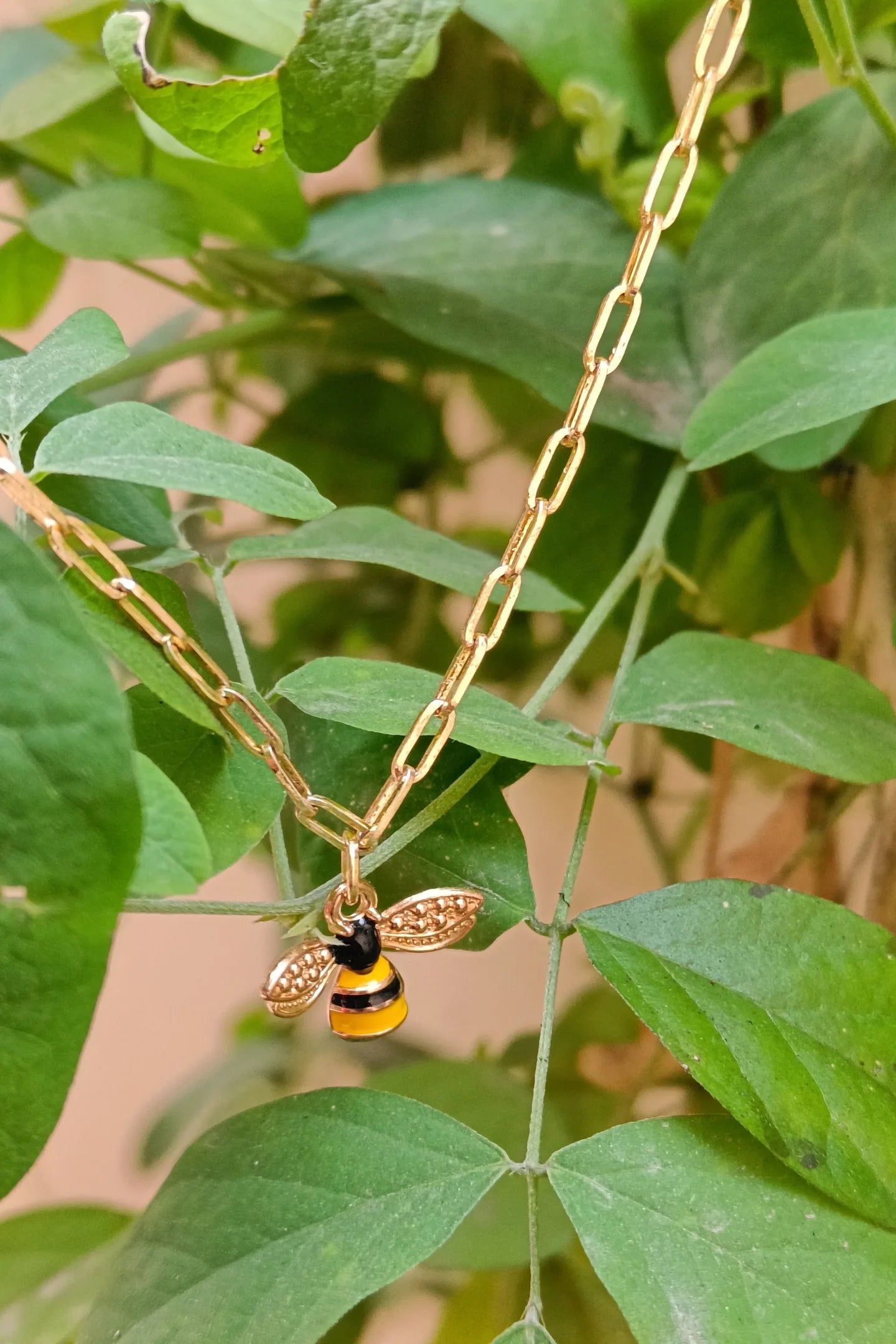 First view of a gold chain necklace with a small pendant shaped like a honey bee.