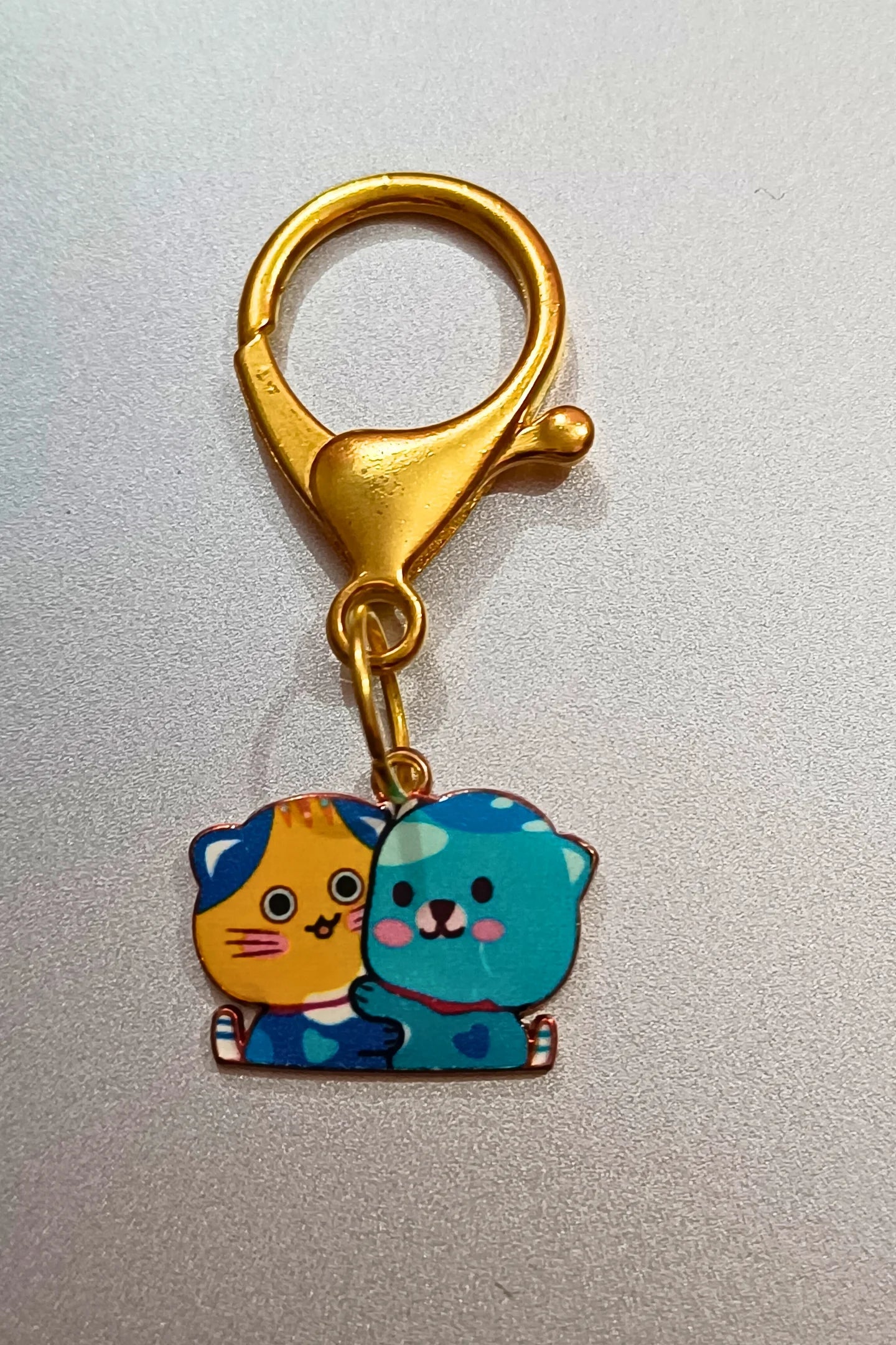 Another view of a couples keychain featuring two separate charms depicting cats hugging each other. The cats' colors may vary, including combinations of pink and blue.