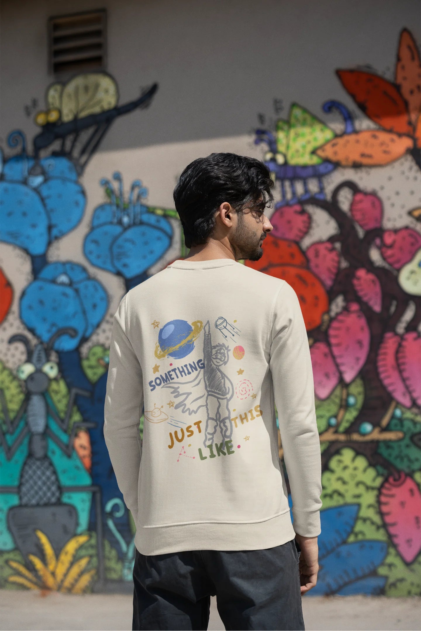 Back view of a male model wearing an cream sweatshirt with a design inspired by the "Something Just Like This" music video, featuring the word "Superheroes".