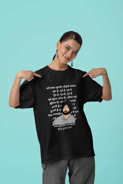 First front view of a female model wearing a black oversized  T-shirt with a Diljit Dosanjh portrait  with lyrics from the song "Ikk Kudi" in the background.