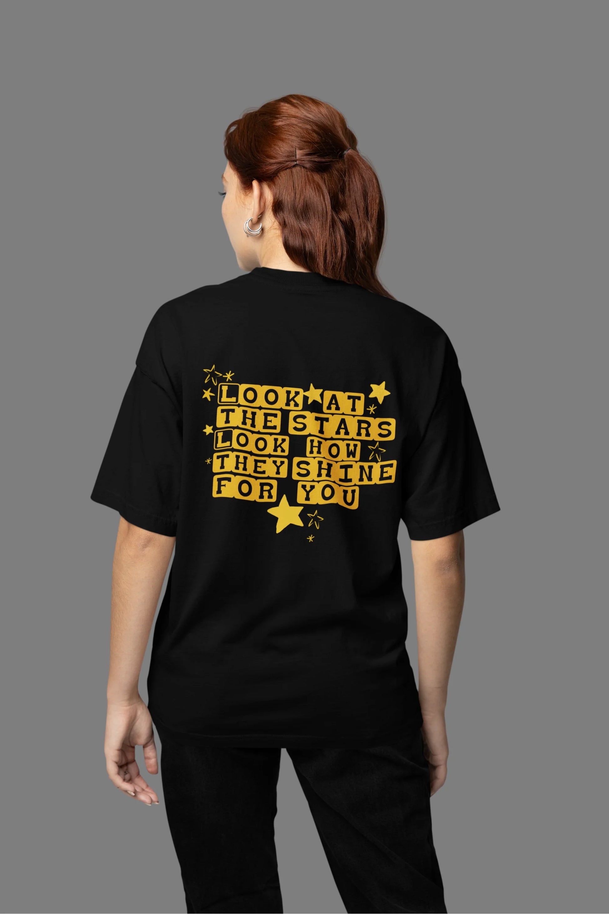 Back view of a female model wearing an black oversized t-shirt with the "Yellow" album artwork by Coldplay.