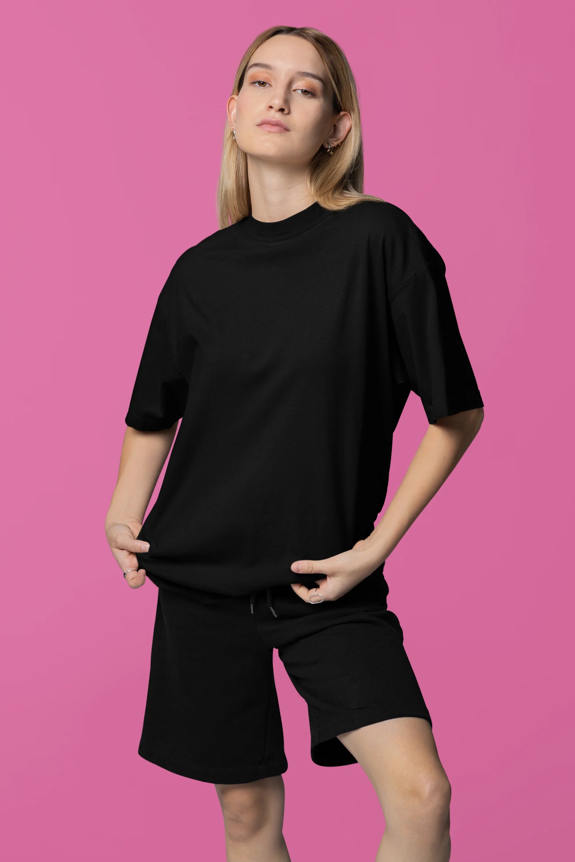 Front view of a female model wearing a black oversized tee with a design of a cat dressed as a samurai, standing against a backdrop of waves and a rising sun.