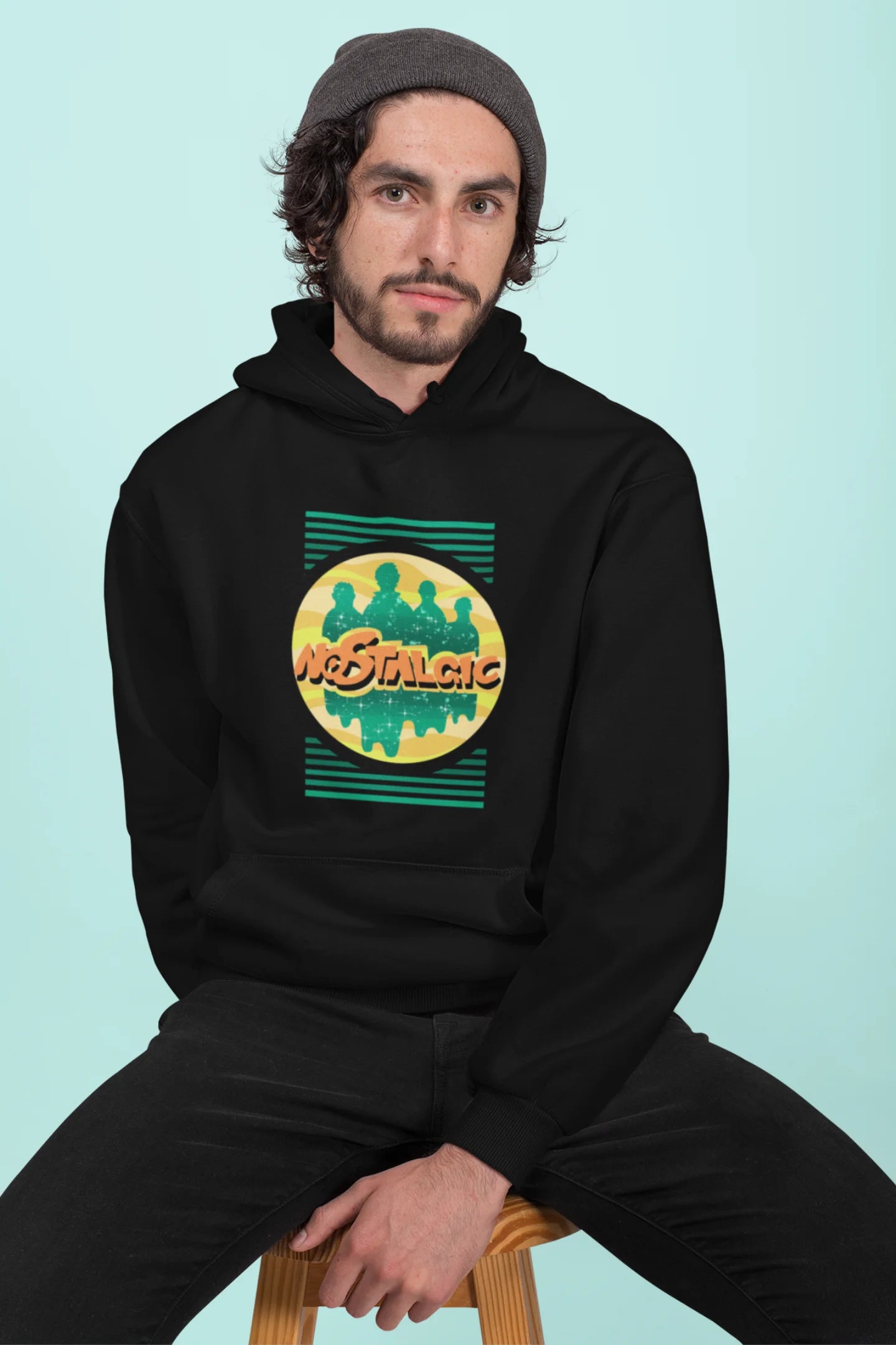 3rd front view of a male model wearing an black hoodie with a shadow silhouette of the Coldplay band members and the word "Nostalgic" printed on it.