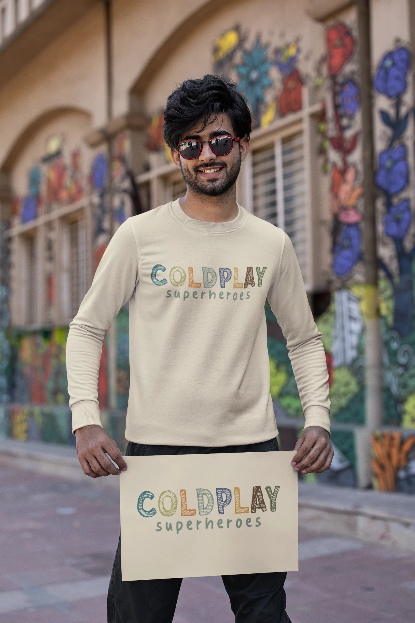 First front view of a male model wearing an cream sweatshirt with a design inspired by the "Something Just Like This" music video, featuring the word "Superheroes".