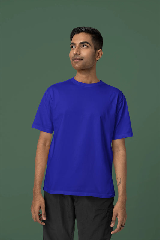 Front view of a male model wearing an oversized royal blue t-shirt featuring a detailed illustration of a gray wolf howling at a full moon in a nighttime setting.