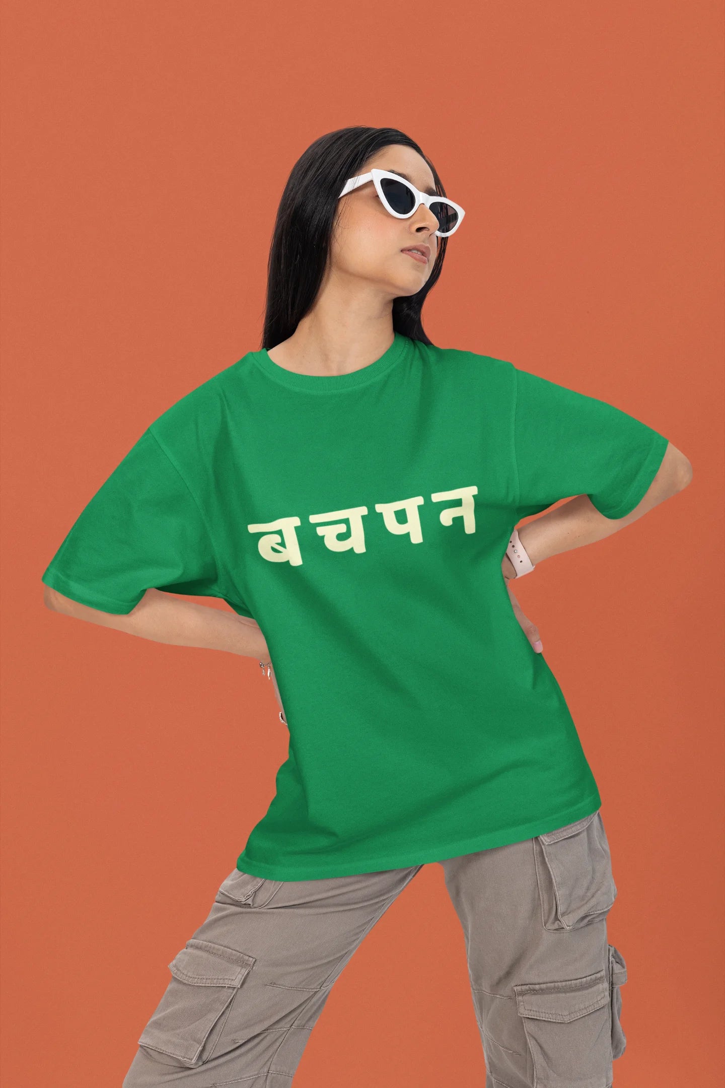 2nd front view of a female model wearing a forest green oversized t-shirt featuring a collage of illustrations or symbols representing various childhood games commonly played by kids in India.