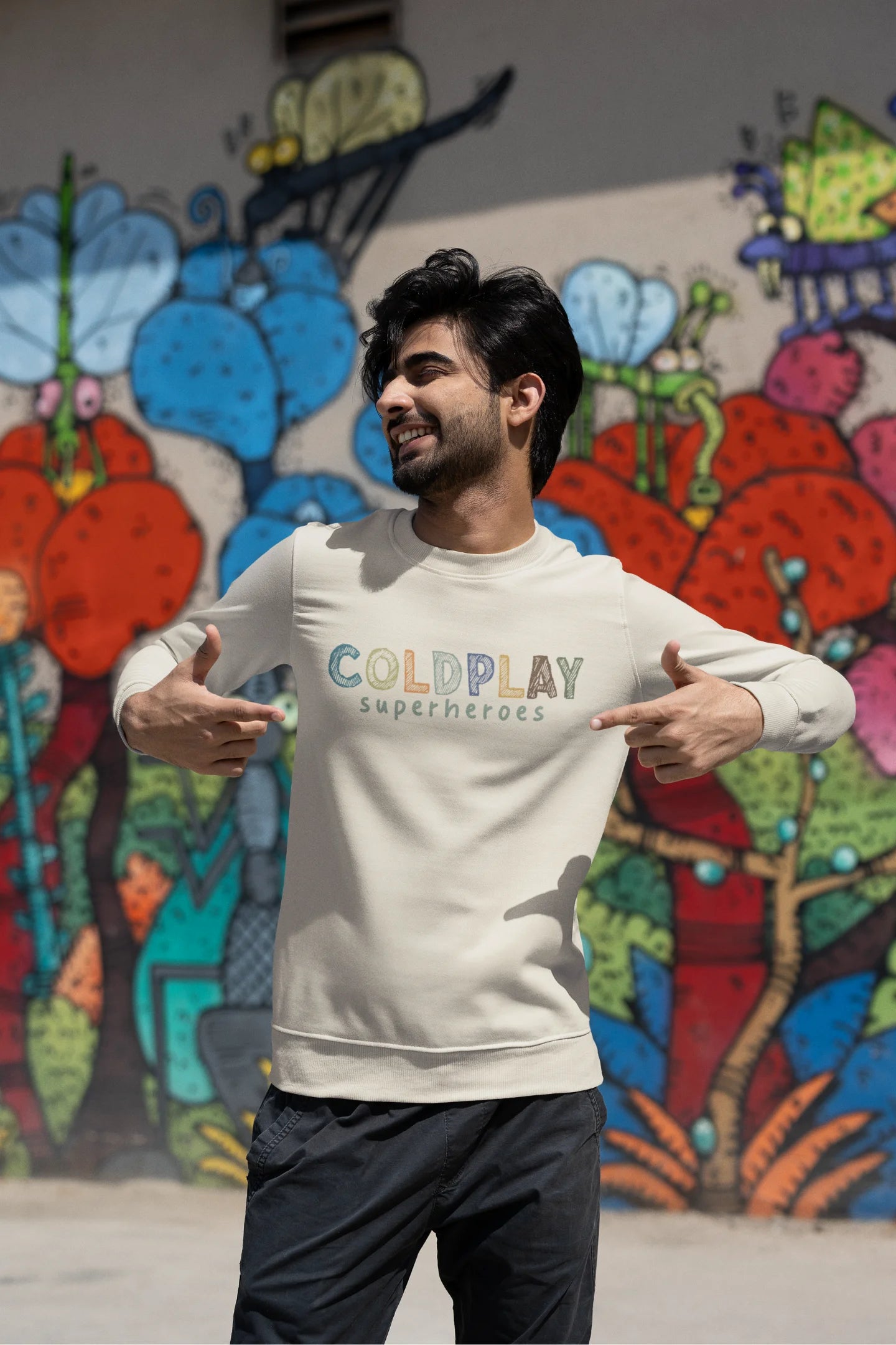 Third front view of a male model wearing an cream sweatshirt with a design inspired by the "Something Just Like This" music video, featuring the word "Superheroes".