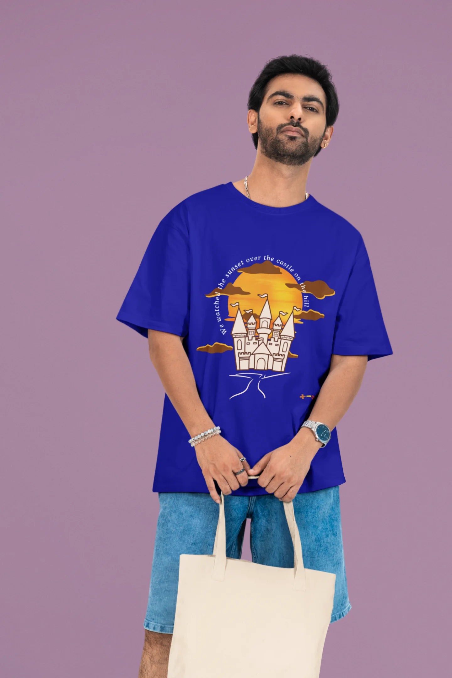 2nd front view of a male model wearing a royal blue oversized t-shirt featuring a nostalgic sunset and castle design, related to Ed Sheeran's "Castle on the Hill."