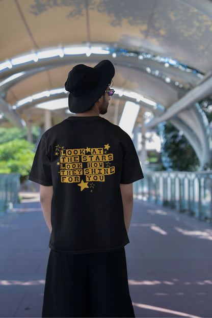 Back view of a male model wearing an black oversized t-shirt with the "Yellow" album artwork by Coldplay.