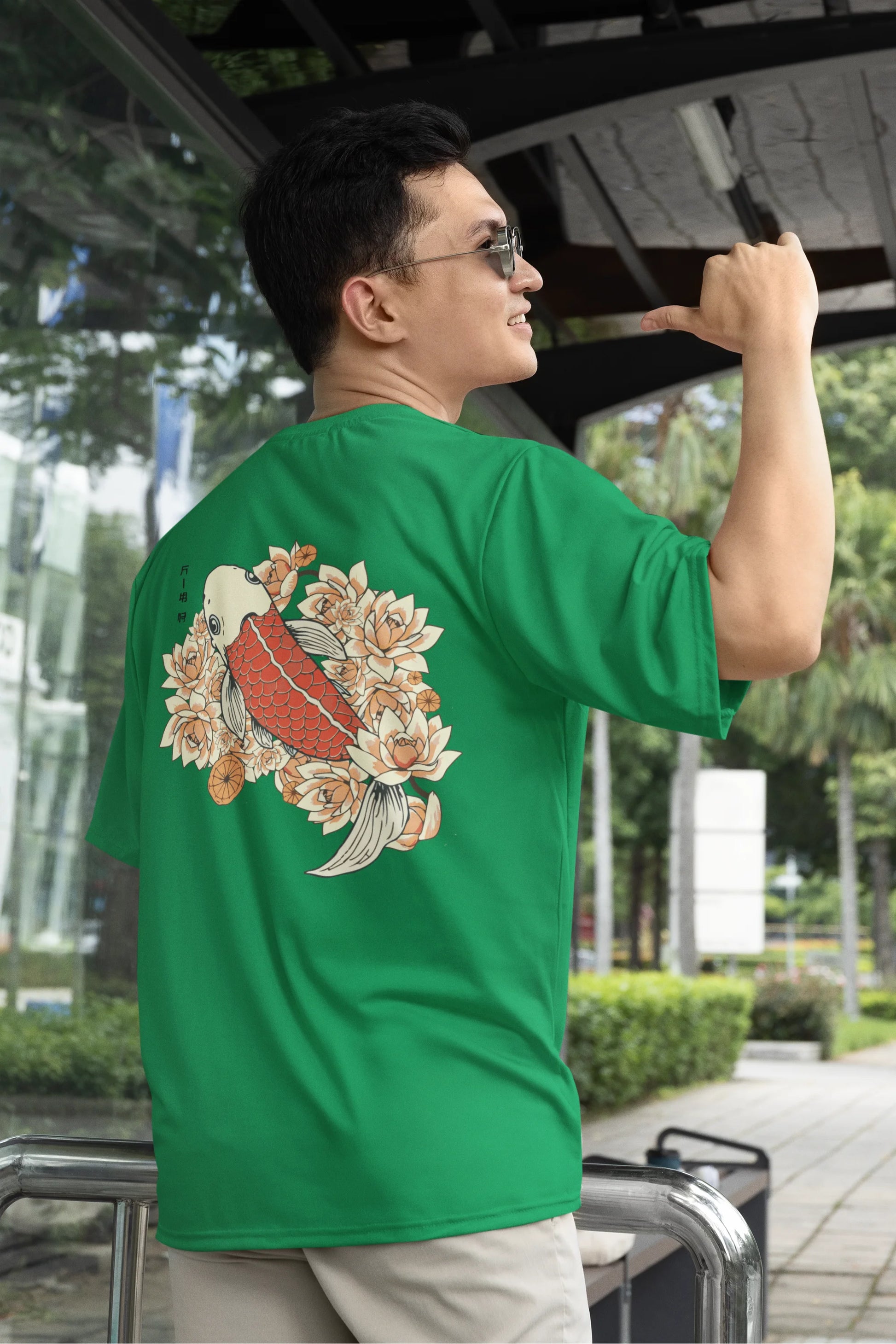 2nd Back view of a male model wearing a forest green oversized tee with a design of a koi fish swimming in a bed of flowers.