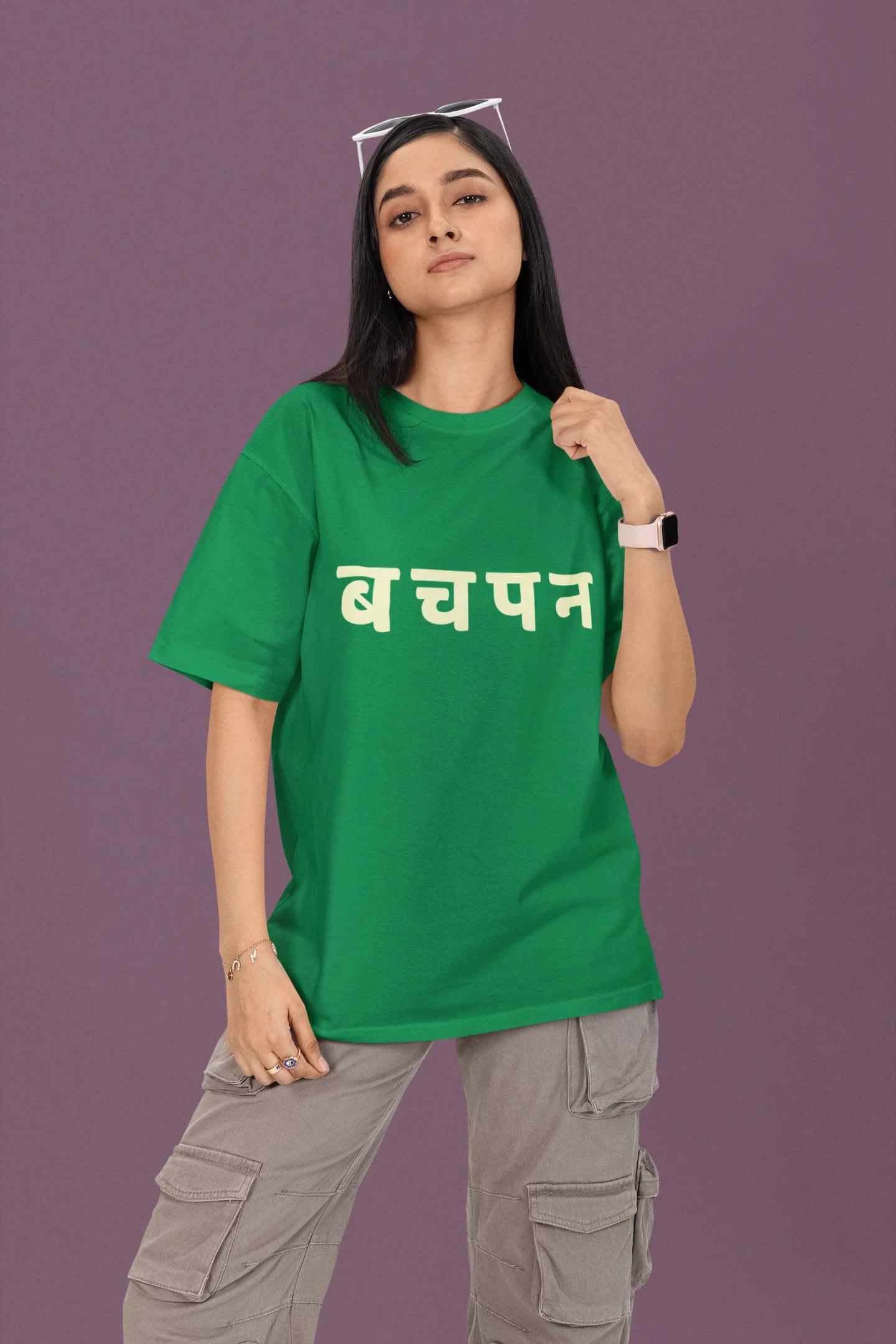First front view of a female model wearing a forest green oversized t-shirt featuring a collage of illustrations or symbols representing various childhood games commonly played by kids in India.