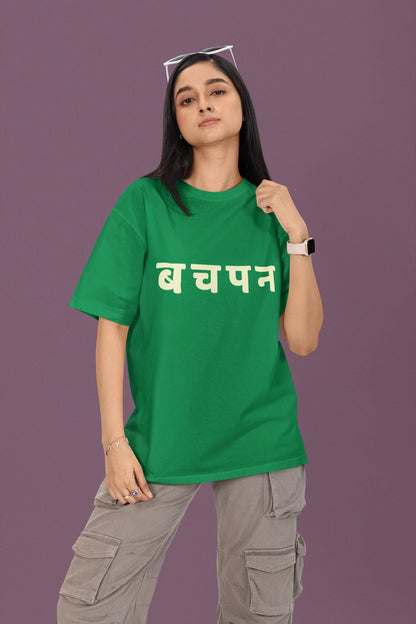 First front view of a female model wearing a forest green oversized t-shirt featuring a collage of illustrations or symbols representing various childhood games commonly played by kids in India.
