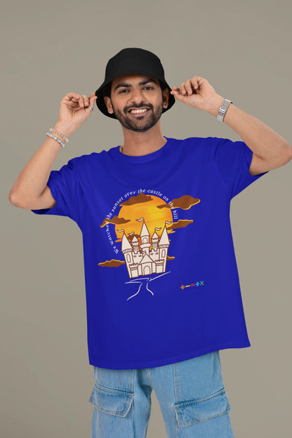 First front view of a male model wearing a royal blue oversized t-shirt featuring a nostalgic sunset and castle design, related to Ed Sheeran's "Castle on the Hill."