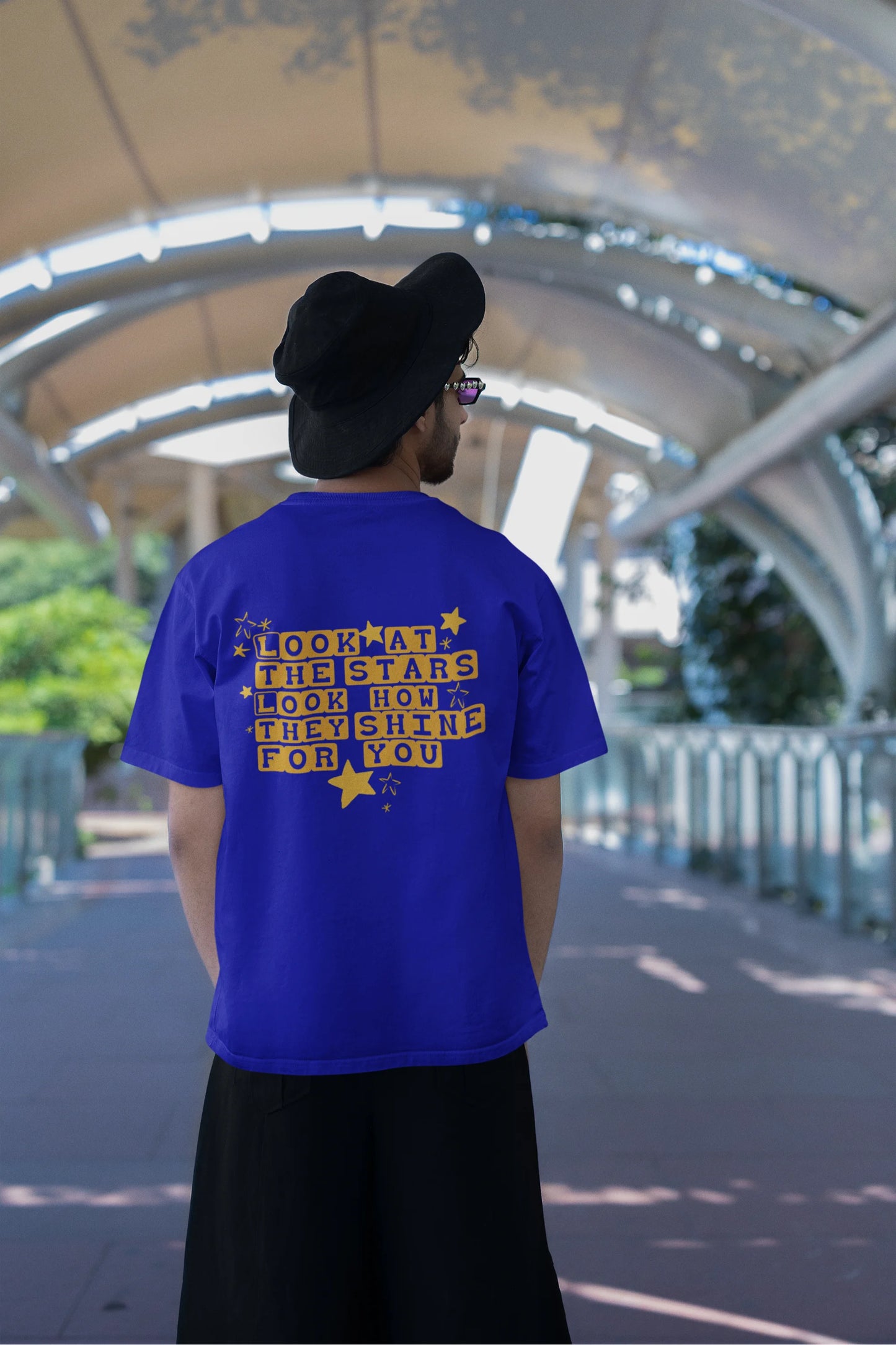 Back view of a male model wearing an royal blue oversized t-shirt with the "Yellow" album artwork by Coldplay.