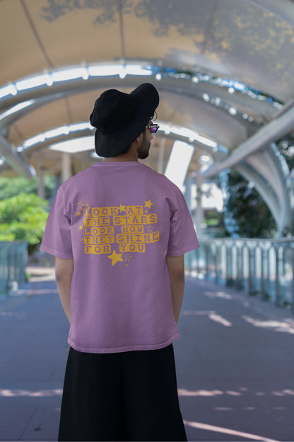Back view of a male model wearing a dirty purple oversized t-shirt with the "Yellow" album artwork by Coldplay.