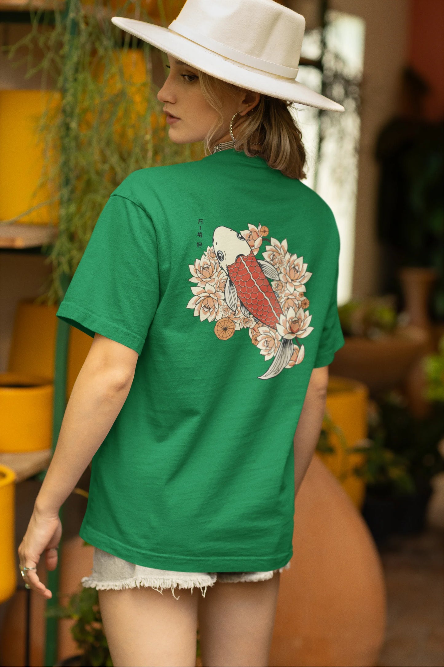 Back view of a female model wearing a forest green oversized tee with a design of a koi fish swimming in a bed of flowers.