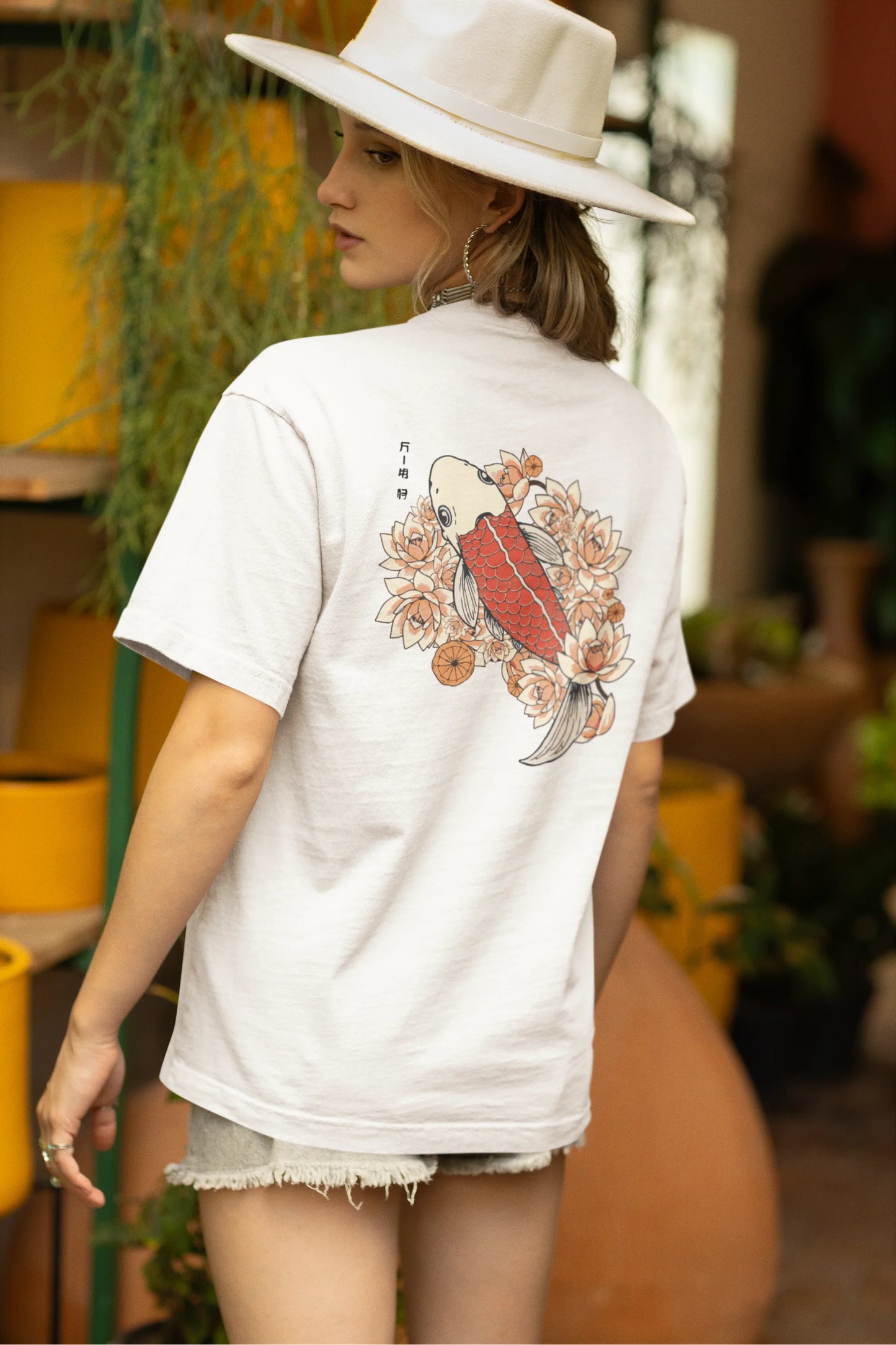 Back view of a female model wearing a off-white oversized tee with a design of a koi fish swimming in a bed of flowers.
