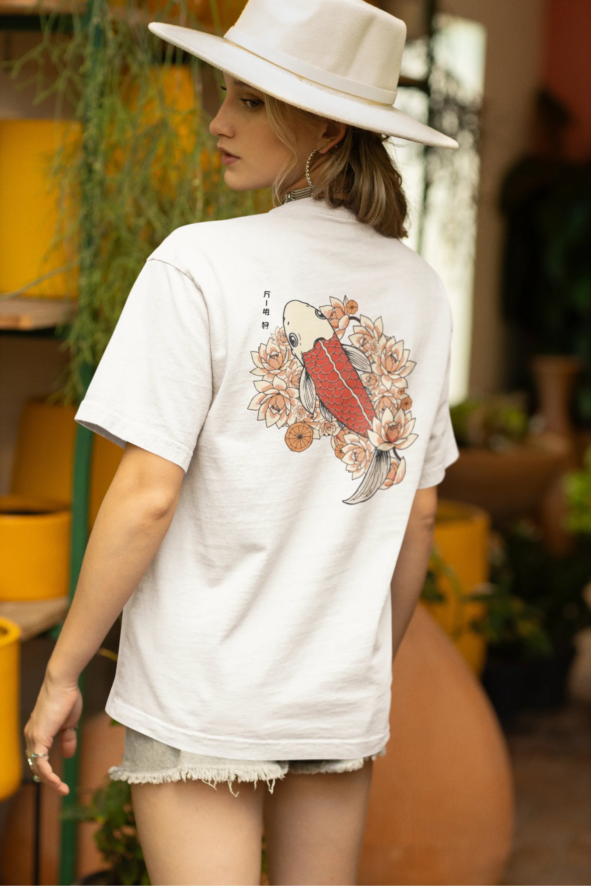 Back view of a female model wearing a off-white oversized tee with a design of a koi fish swimming in a bed of flowers.