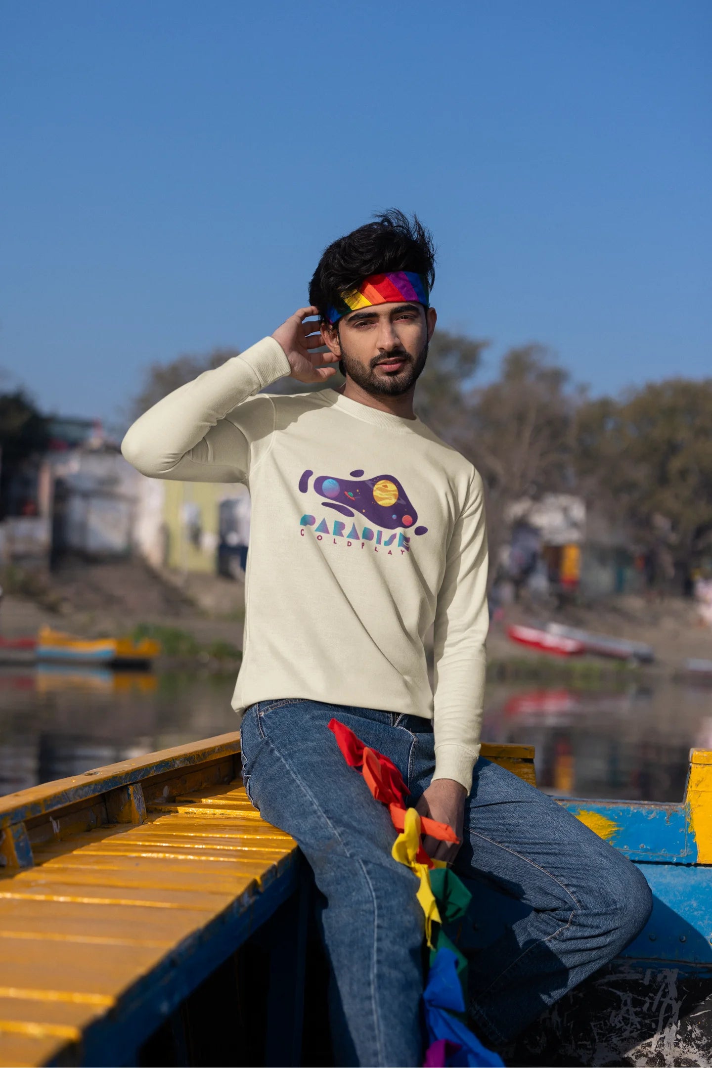 Third front view of a male model wearing an cream sweatshirt with the "Paradise" album artwork by Coldplay.